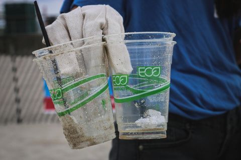 gloved sanitation worker holding plastic cups with the words eco printed in green font with green and blue design
