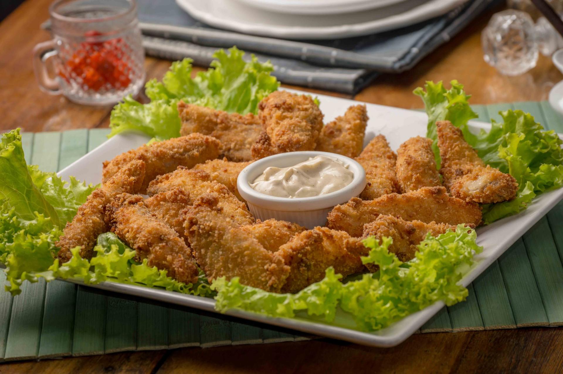 A plate of fried chicken with lettuce and sauce on a table.
