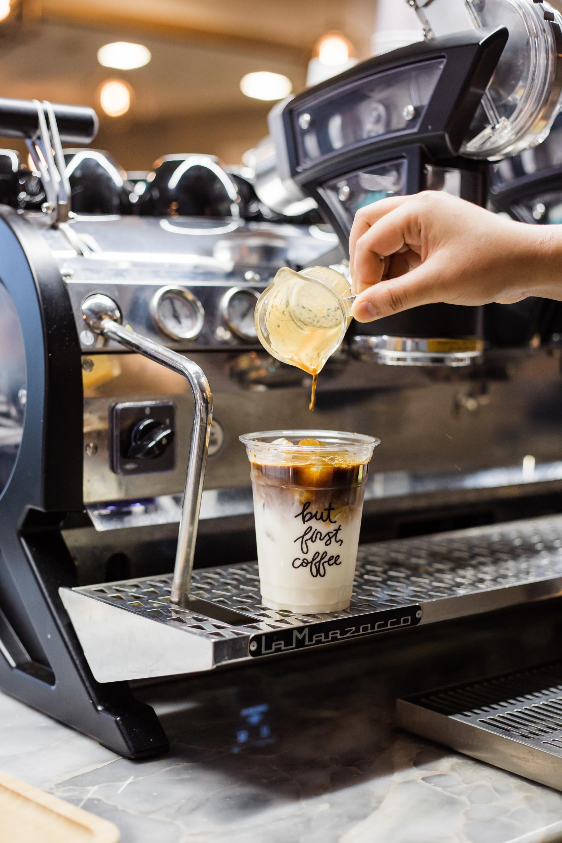 A person is pouring liquid into a cup of iced coffee.