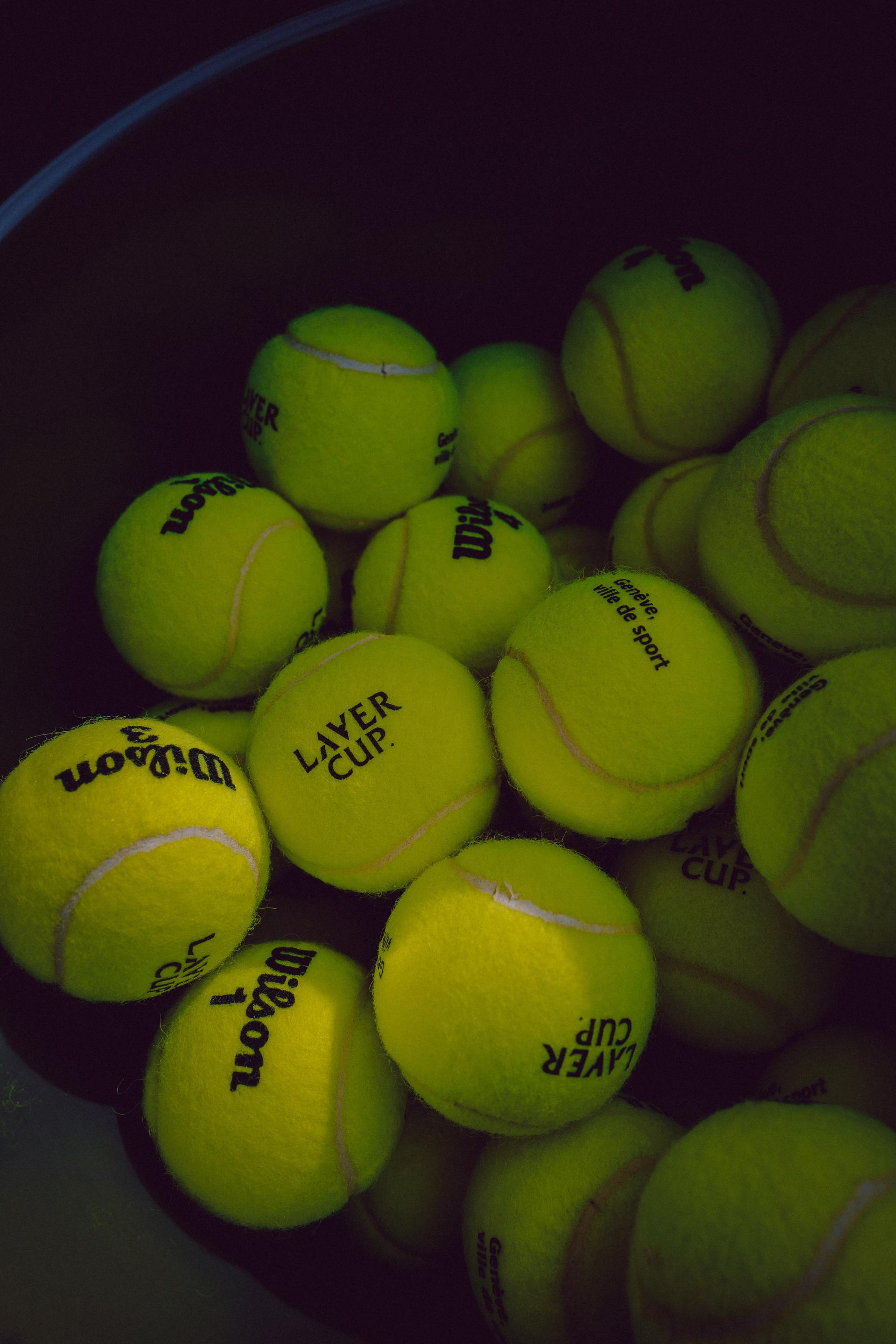 A bucket overflowing with bright yellow tennis balls, some labeled