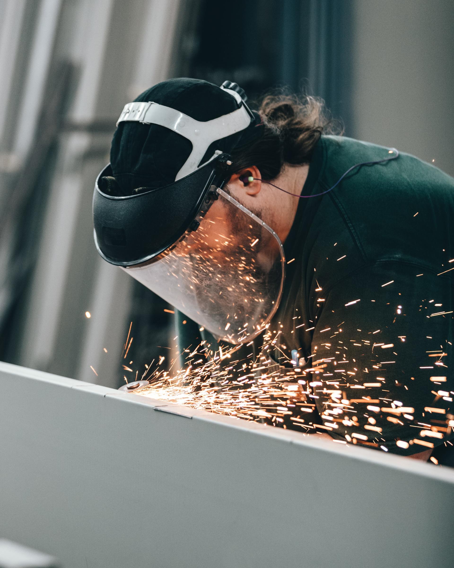 A man wearing a welding mask is grinding a piece of metal.