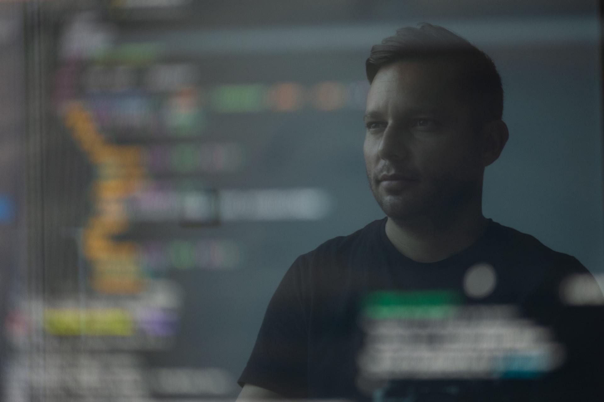A man with a beard is standing in front of a computer screen displaying custom software or firmware.