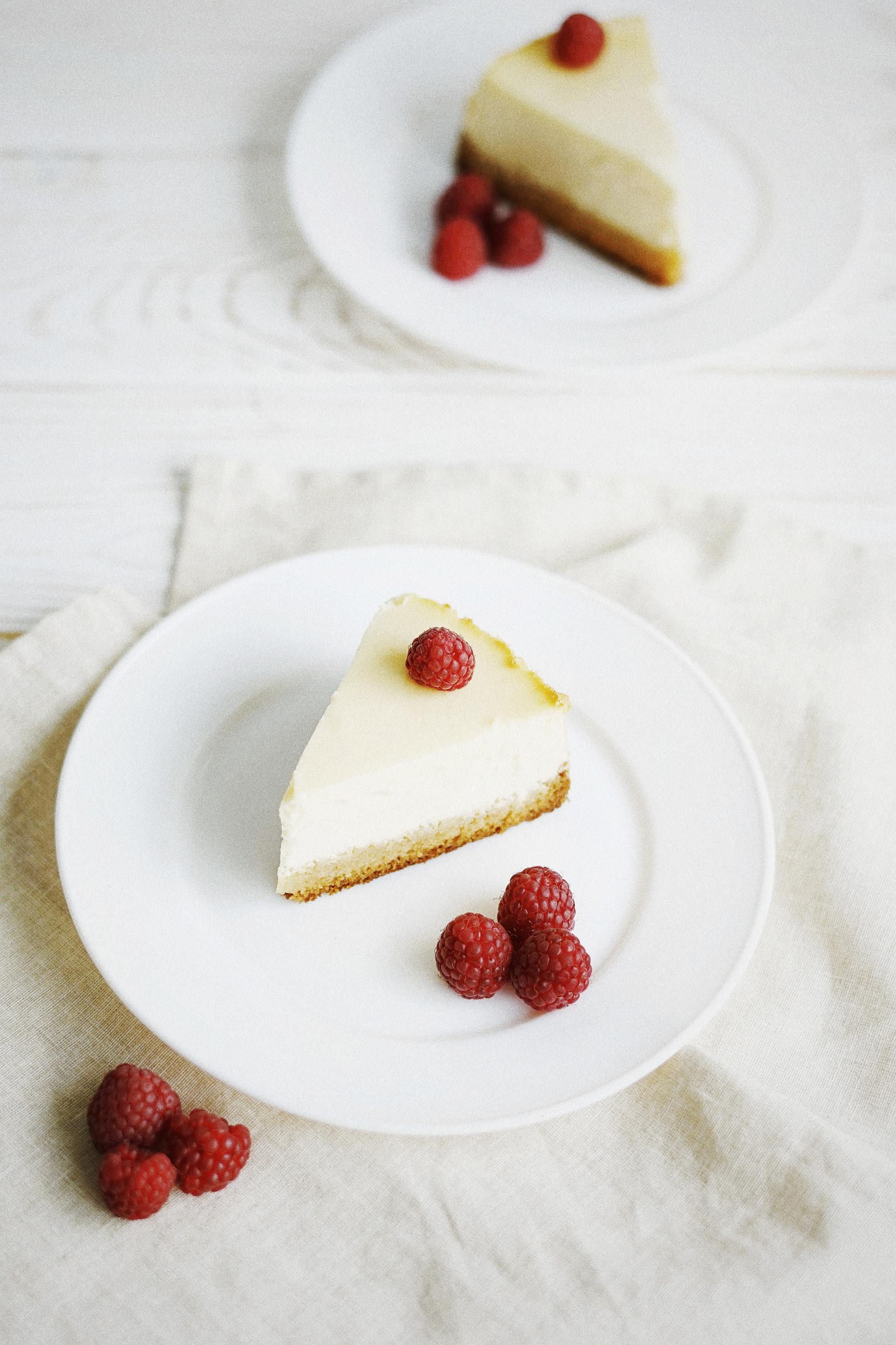 Two white plates topped with slices of cheesecake and raspberries.