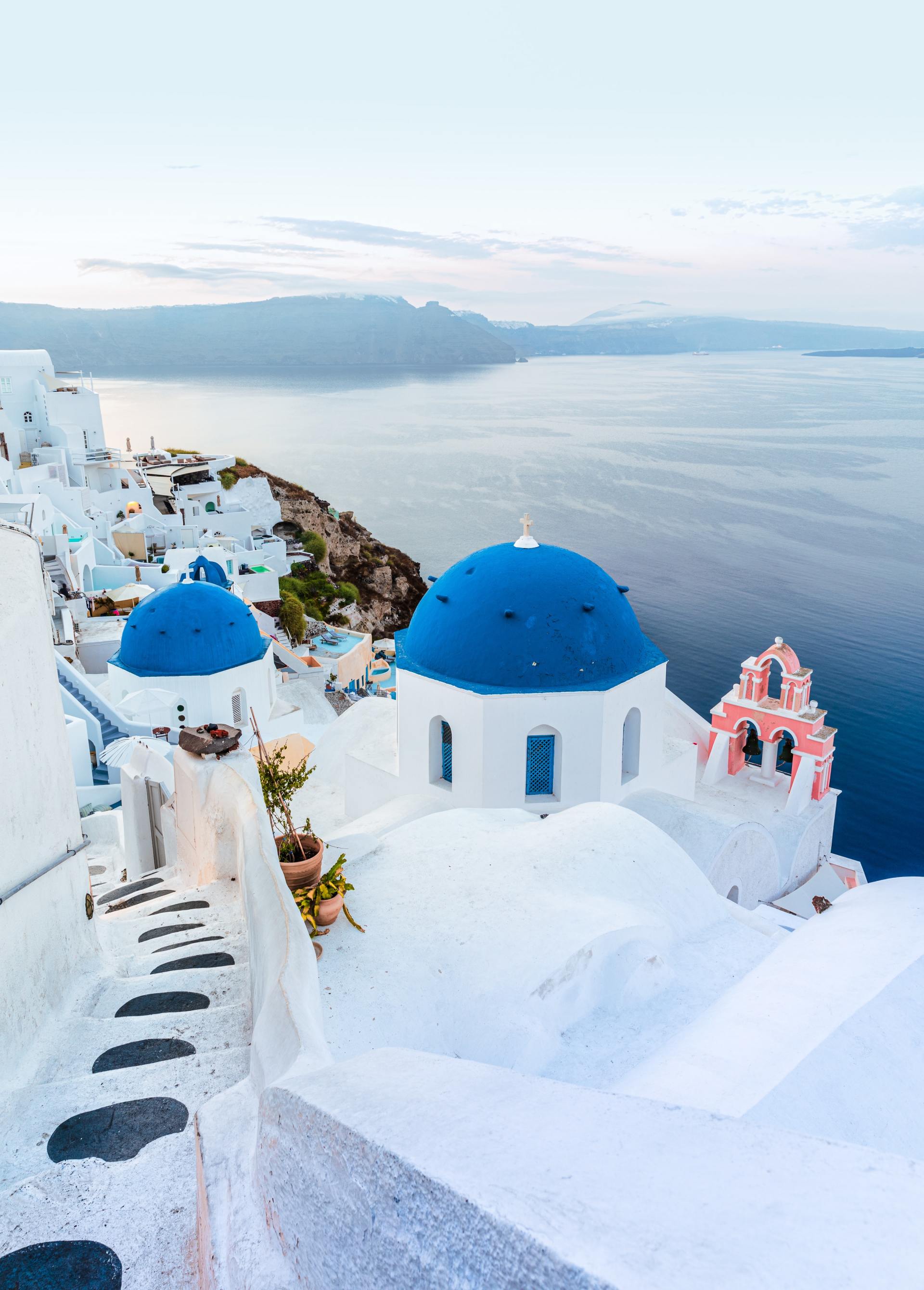 A view of santorini with blue dome buildings and a bell tower overlooking the ocean.