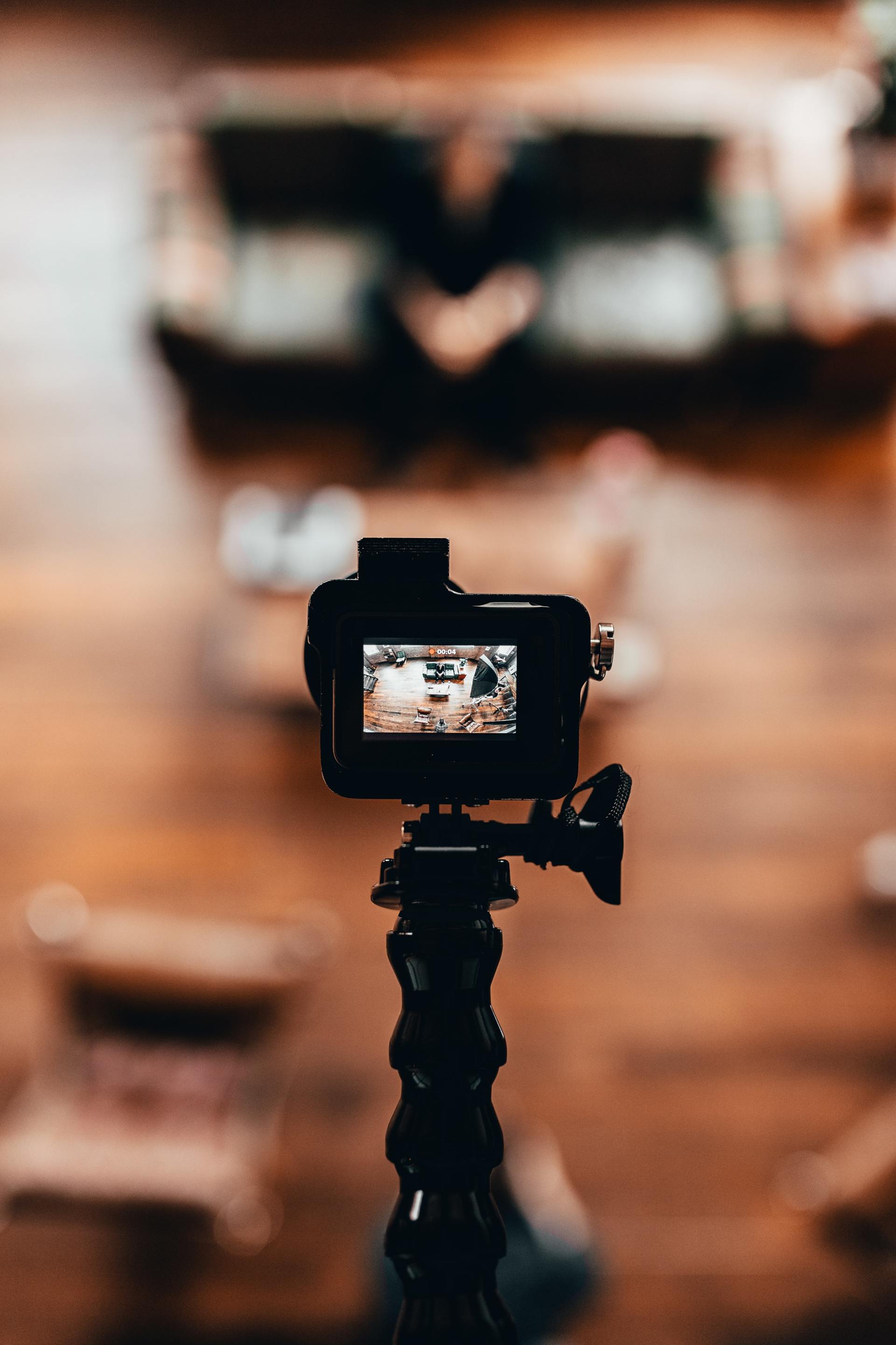 A camera is sitting on a tripod in front of a wooden table.