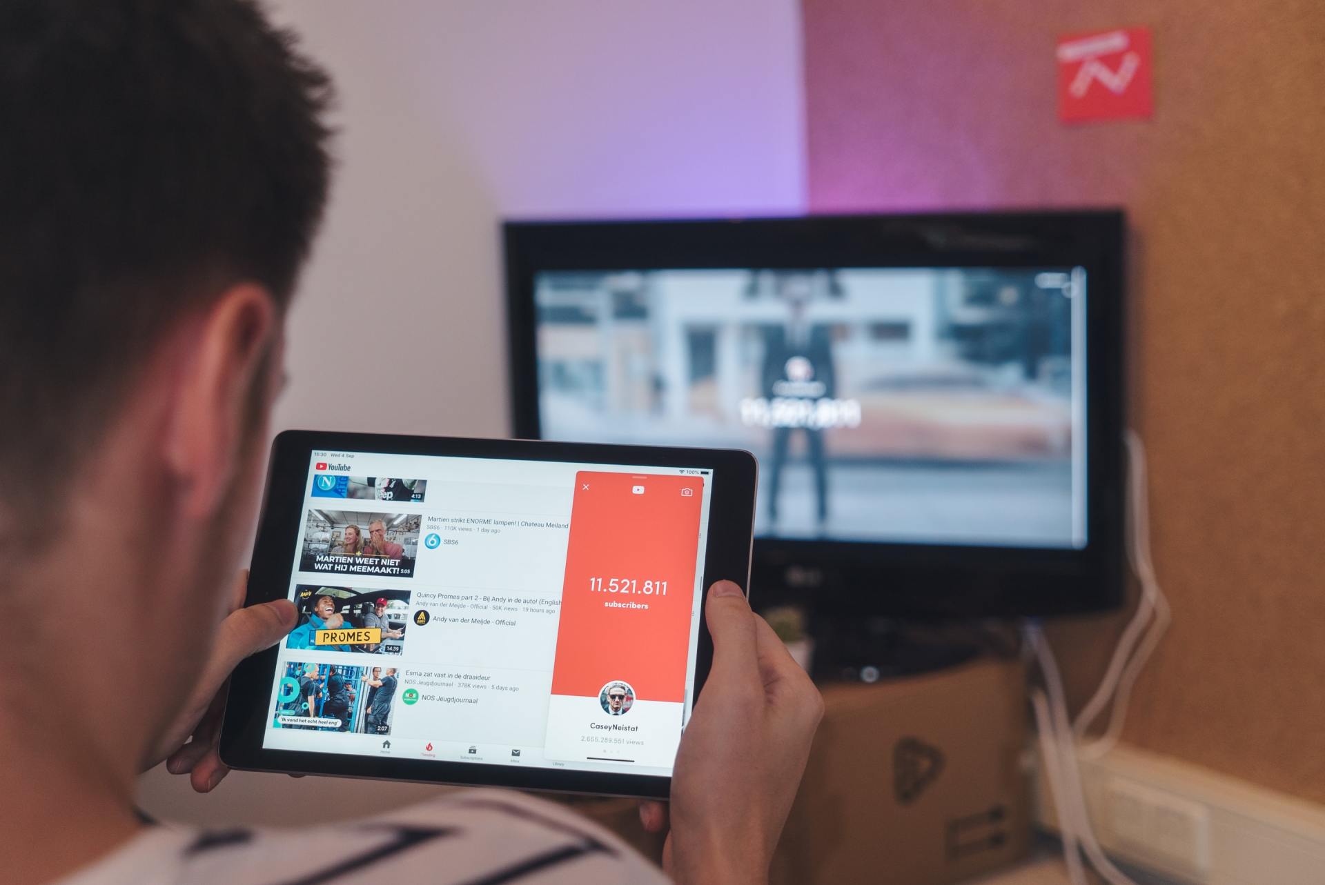 A man is holding a tablet in front of a television.