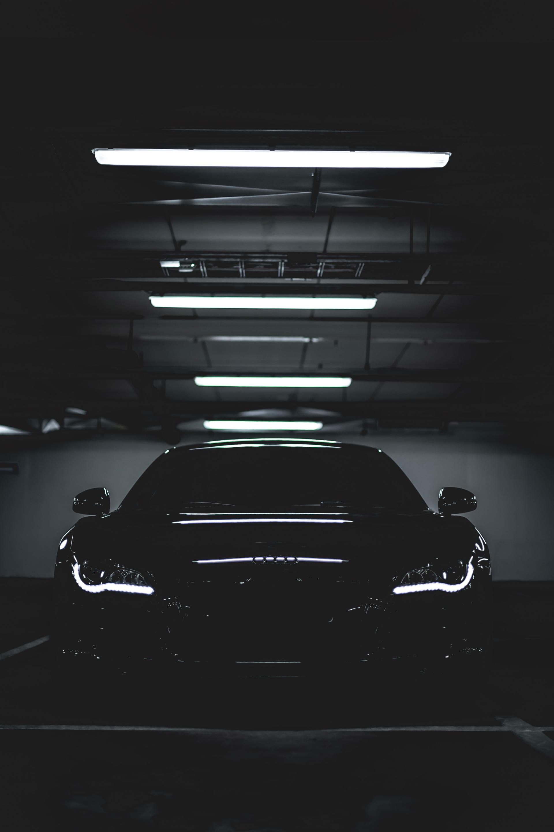A black car is parked in a dark parking garage.