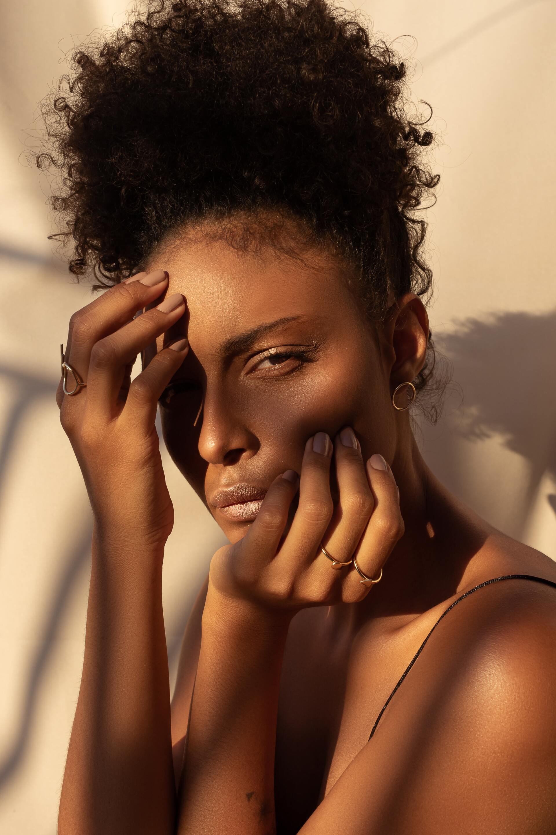 A woman with curly hair is covering her face with her hands.