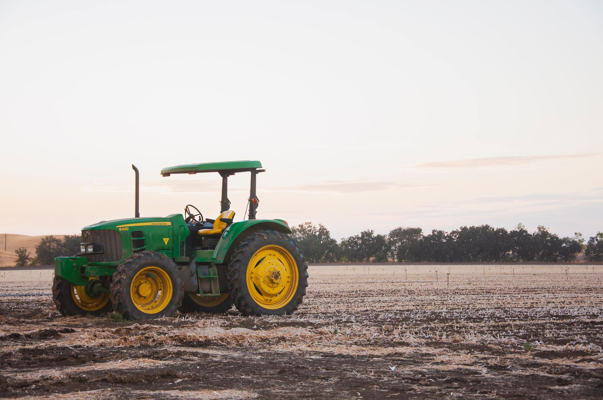 a green and yellow tractor is parked in a dirt field .