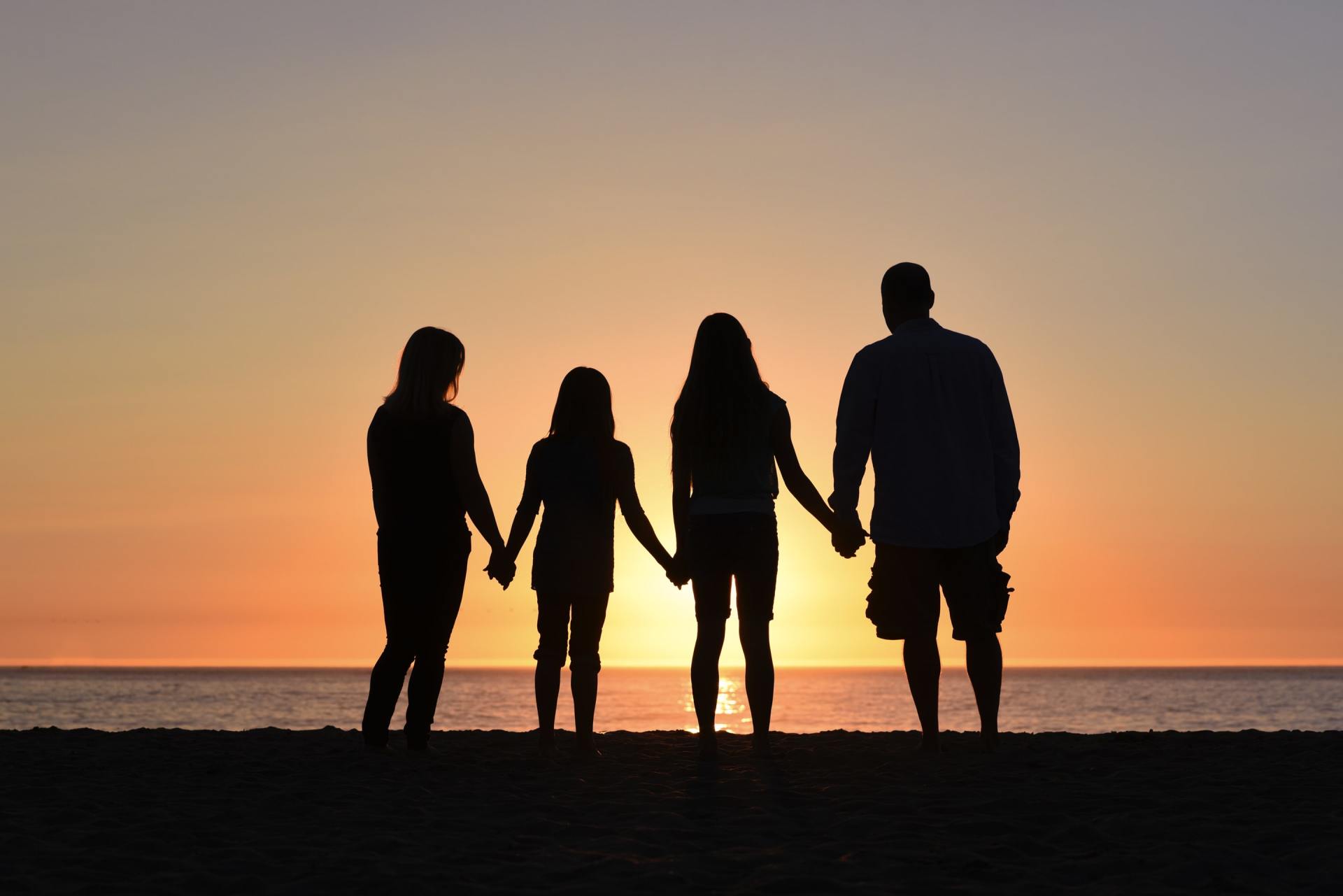 A family is standing on the beach holding hands at sunset.