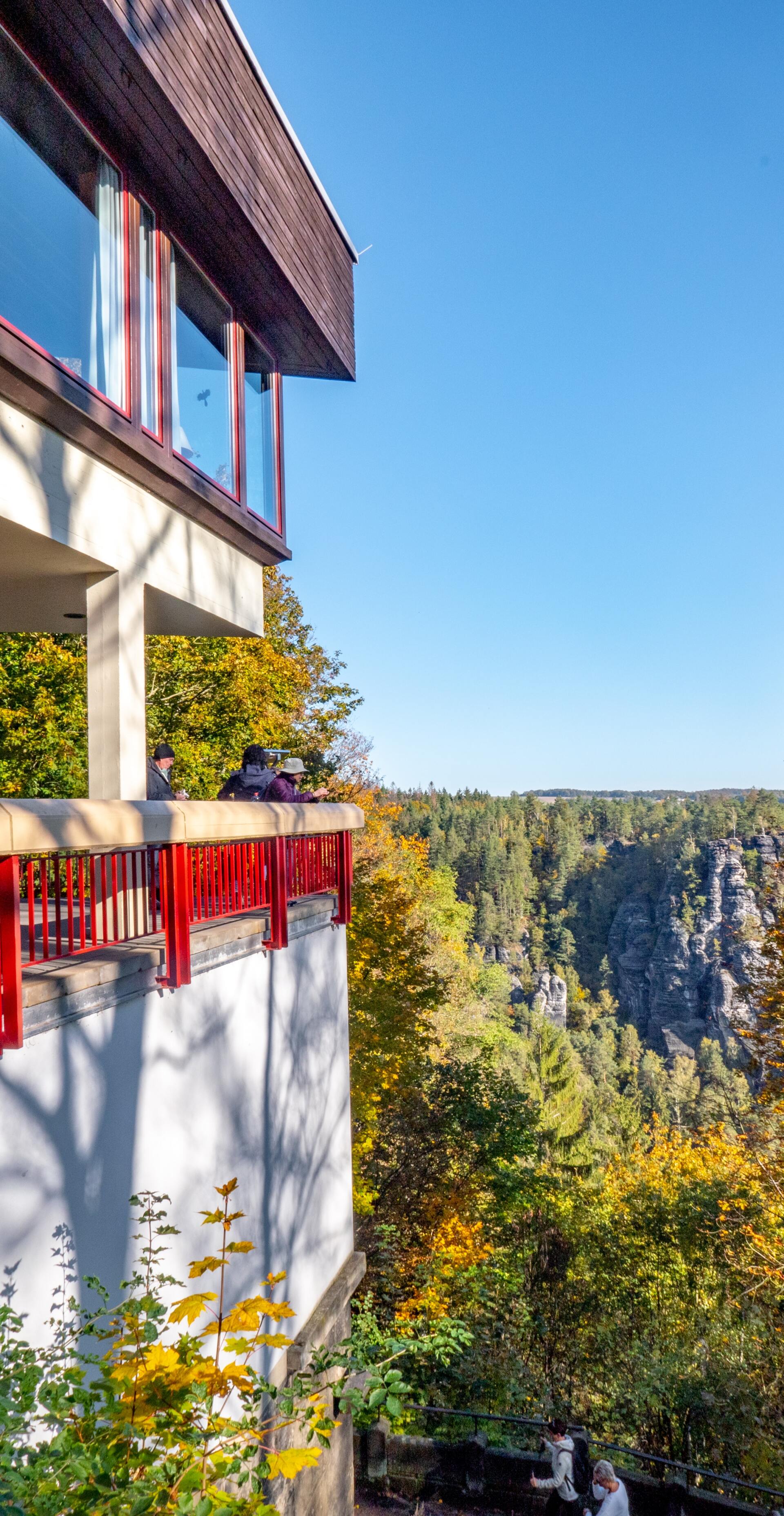 A building with a balcony overlooking a valley surrounded by trees.