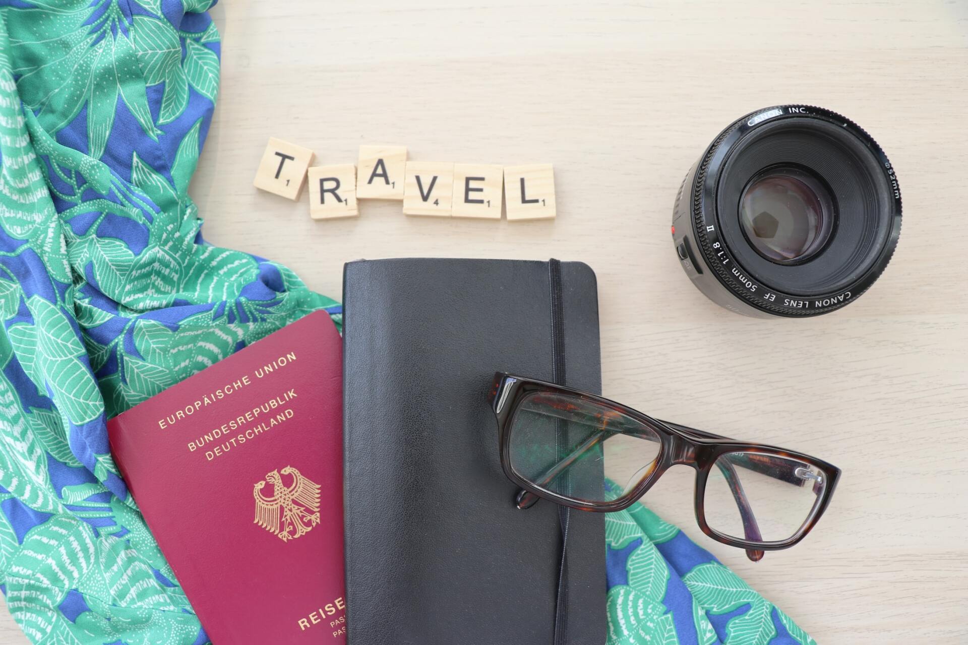 A passport , glasses , a camera and a notebook are on a table.