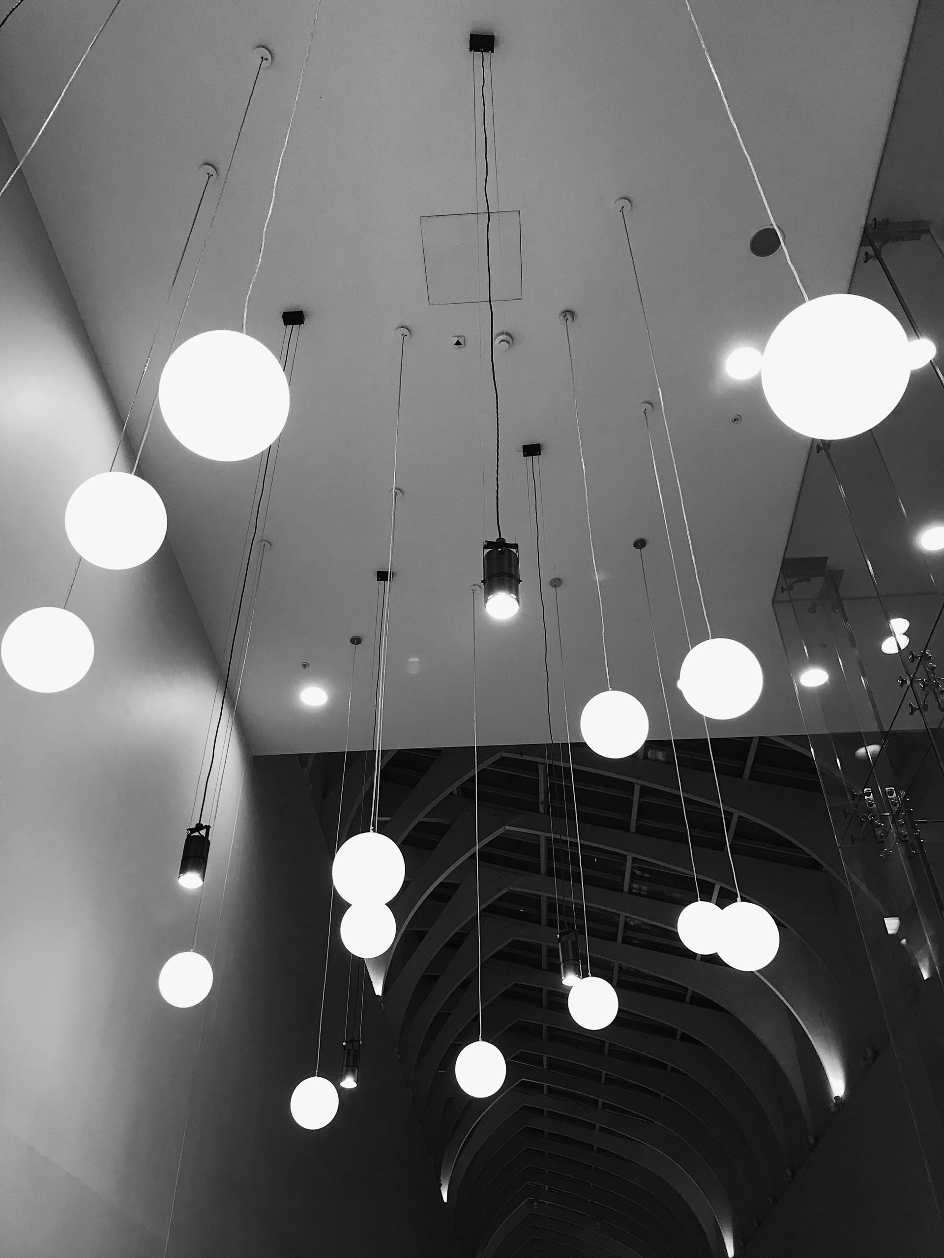 Photo en noir et blanc d'un plafond avec des globes lumineux suspendus et des spots encastrés.