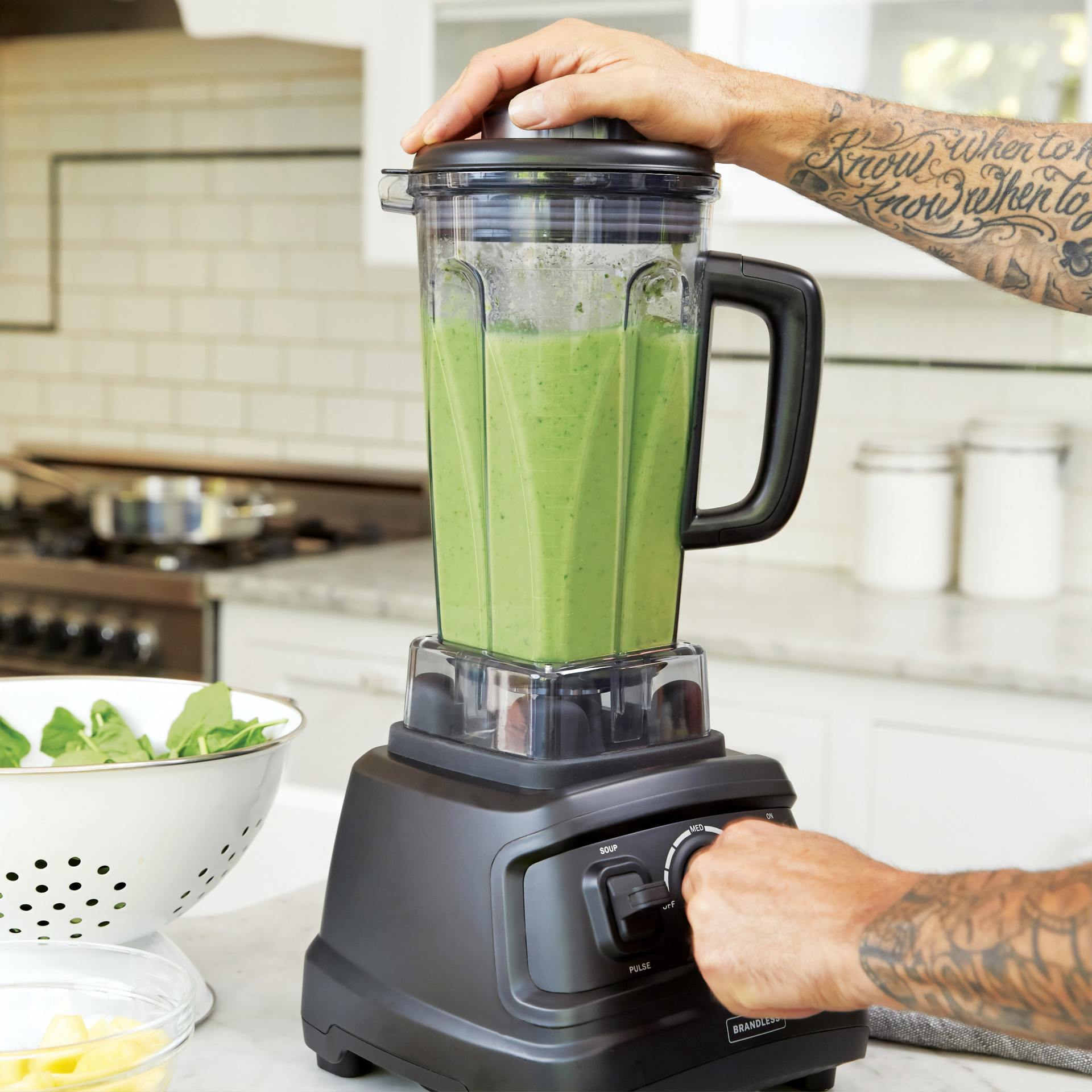 A person with a tattoo on their arm is using a blender to make a green smoothie