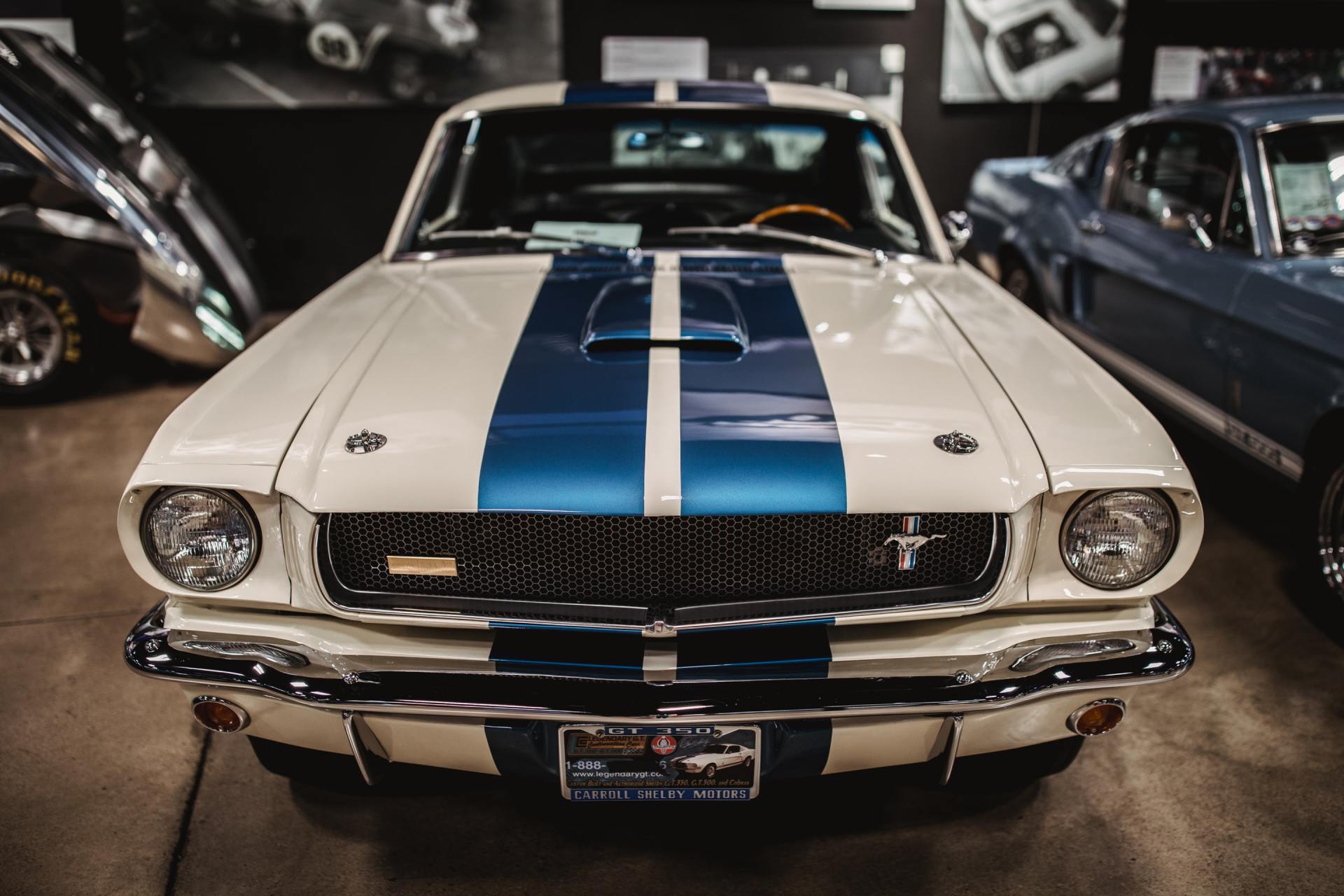 A white mustang with blue stripes is parked in a garage.