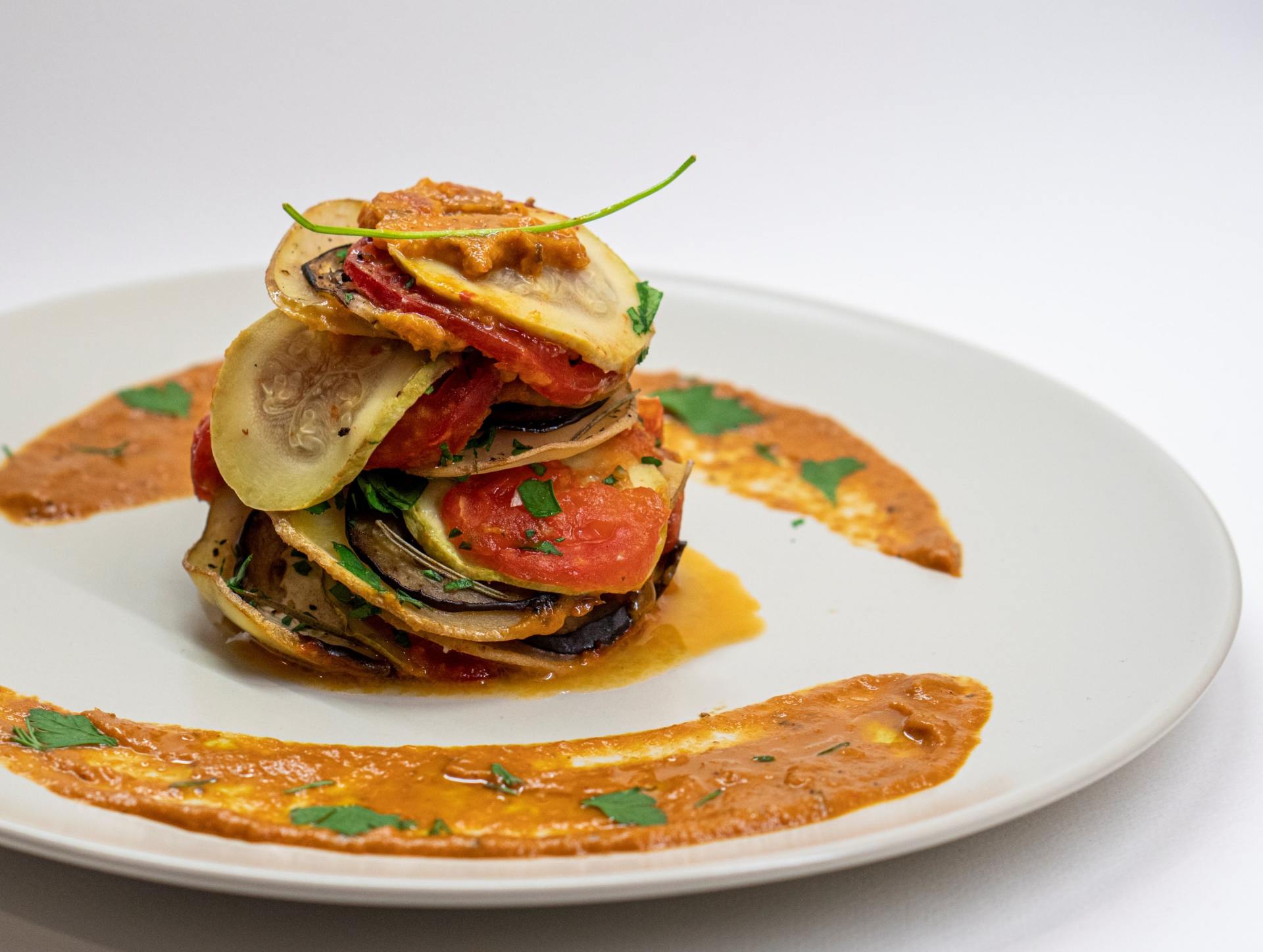 A white plate topped with a stack of vegetables and sauce.