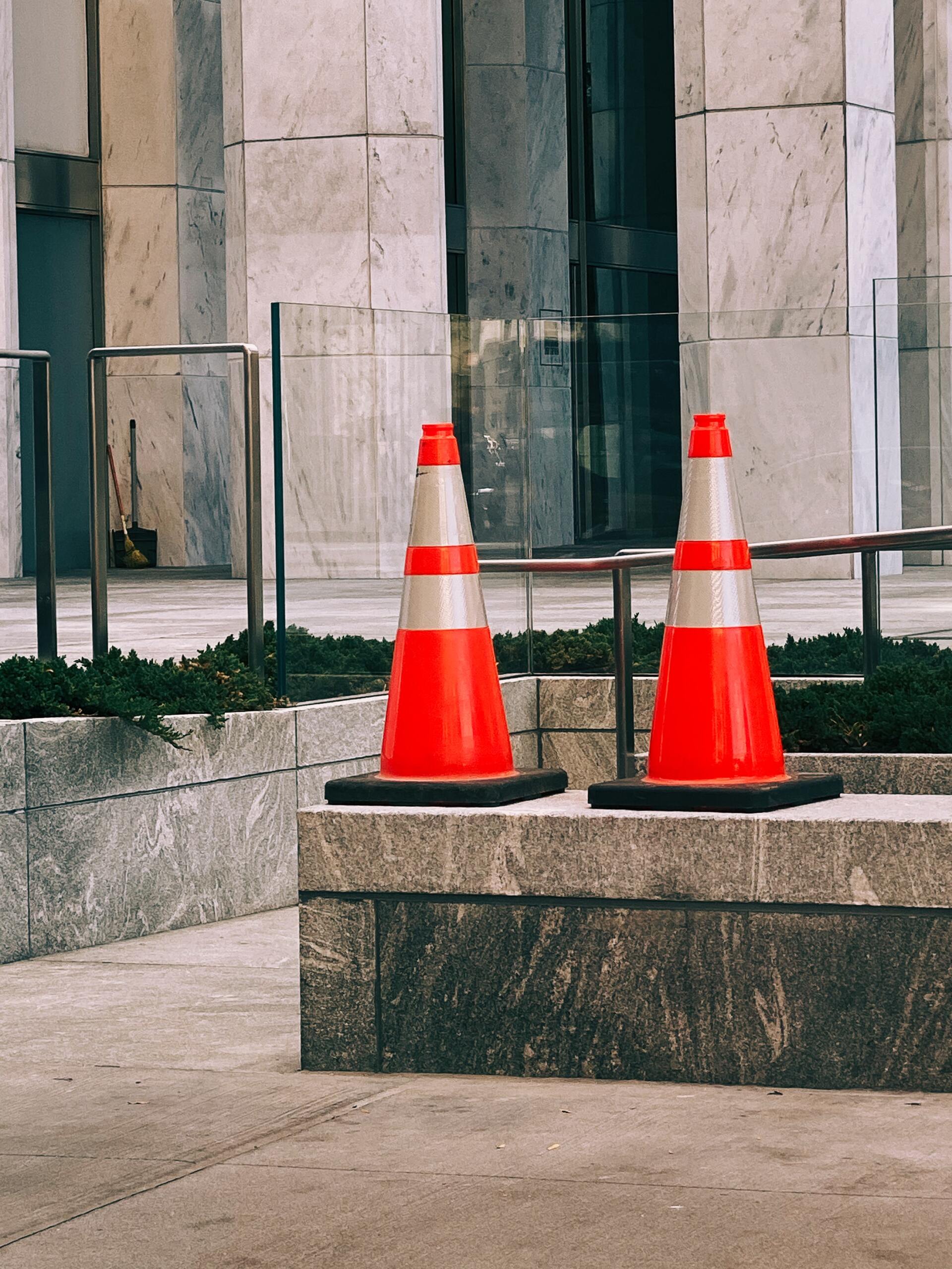 Two orange and white traffic cones are sitting on a sidewalk in front of a building