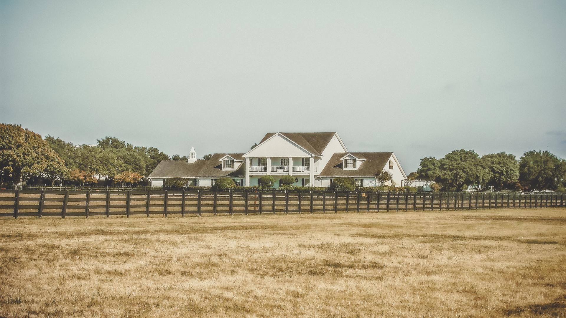 a large white house is behind a wooden fence in a field .