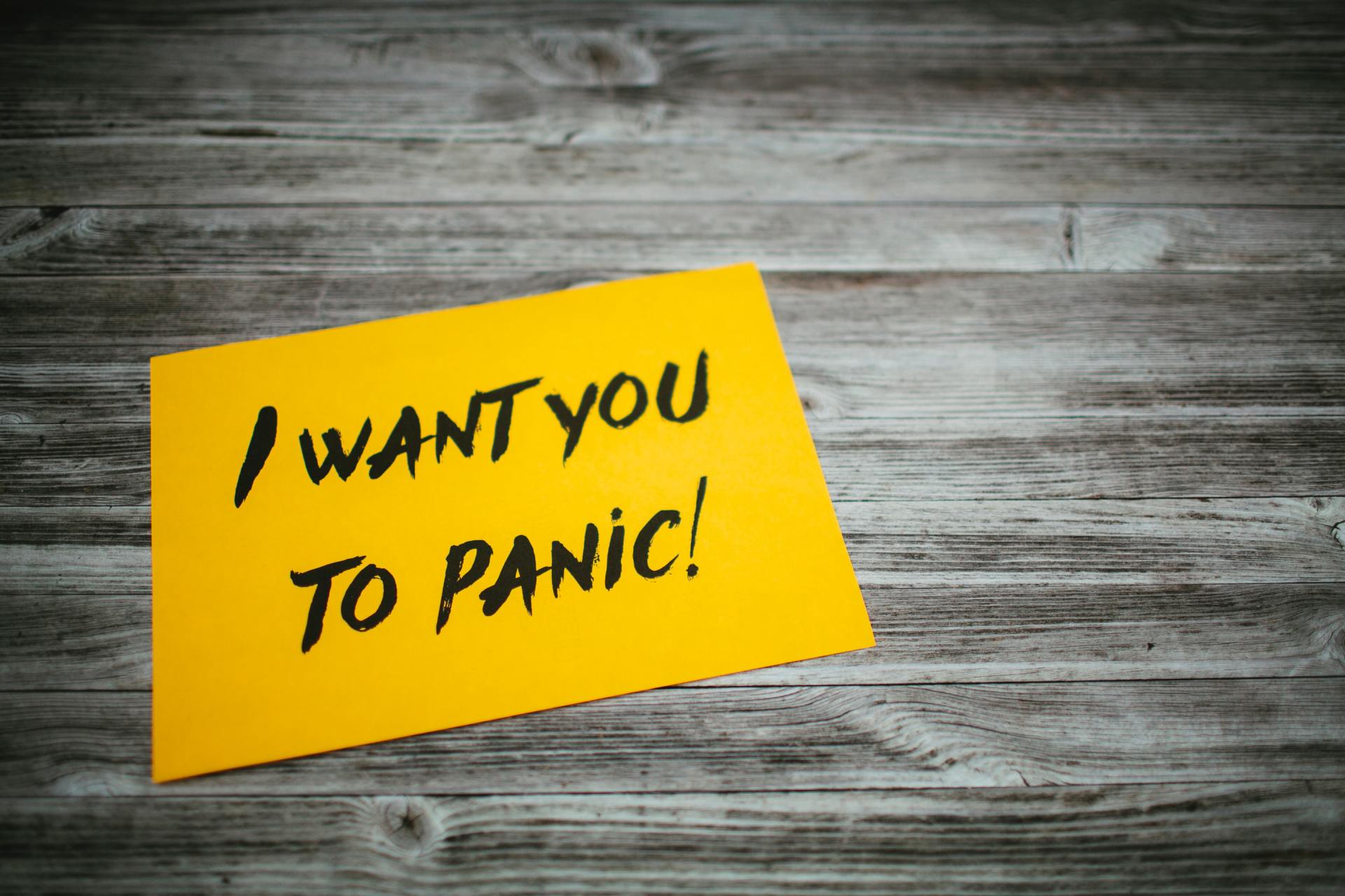 A yellow sticky note on a wooden table that says `` i want you to panic ''.