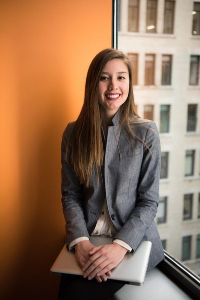 Picture of a woman sitting by a window sill  of a building smiling at the camera