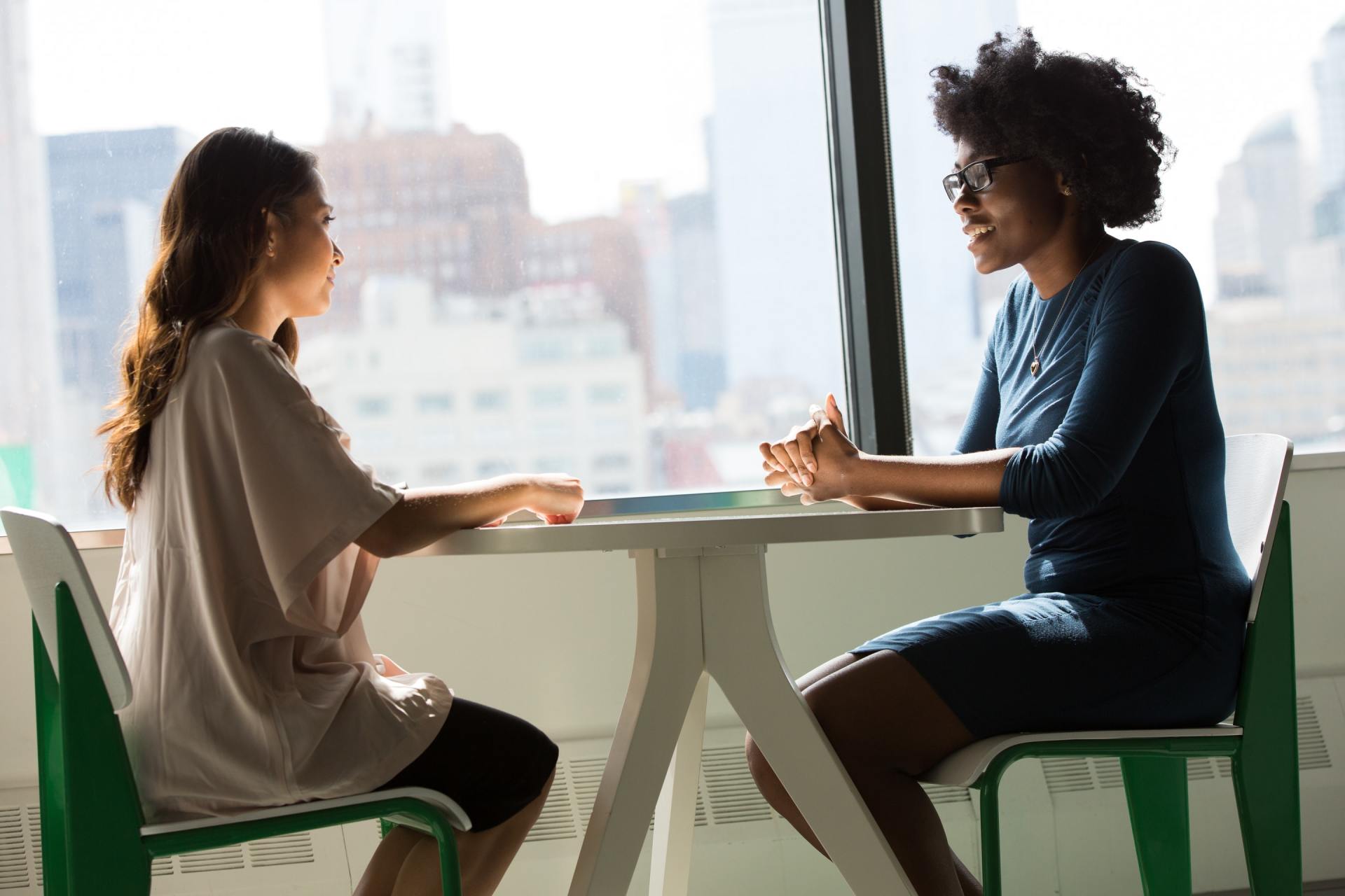 Two women sitting at a desk talking.