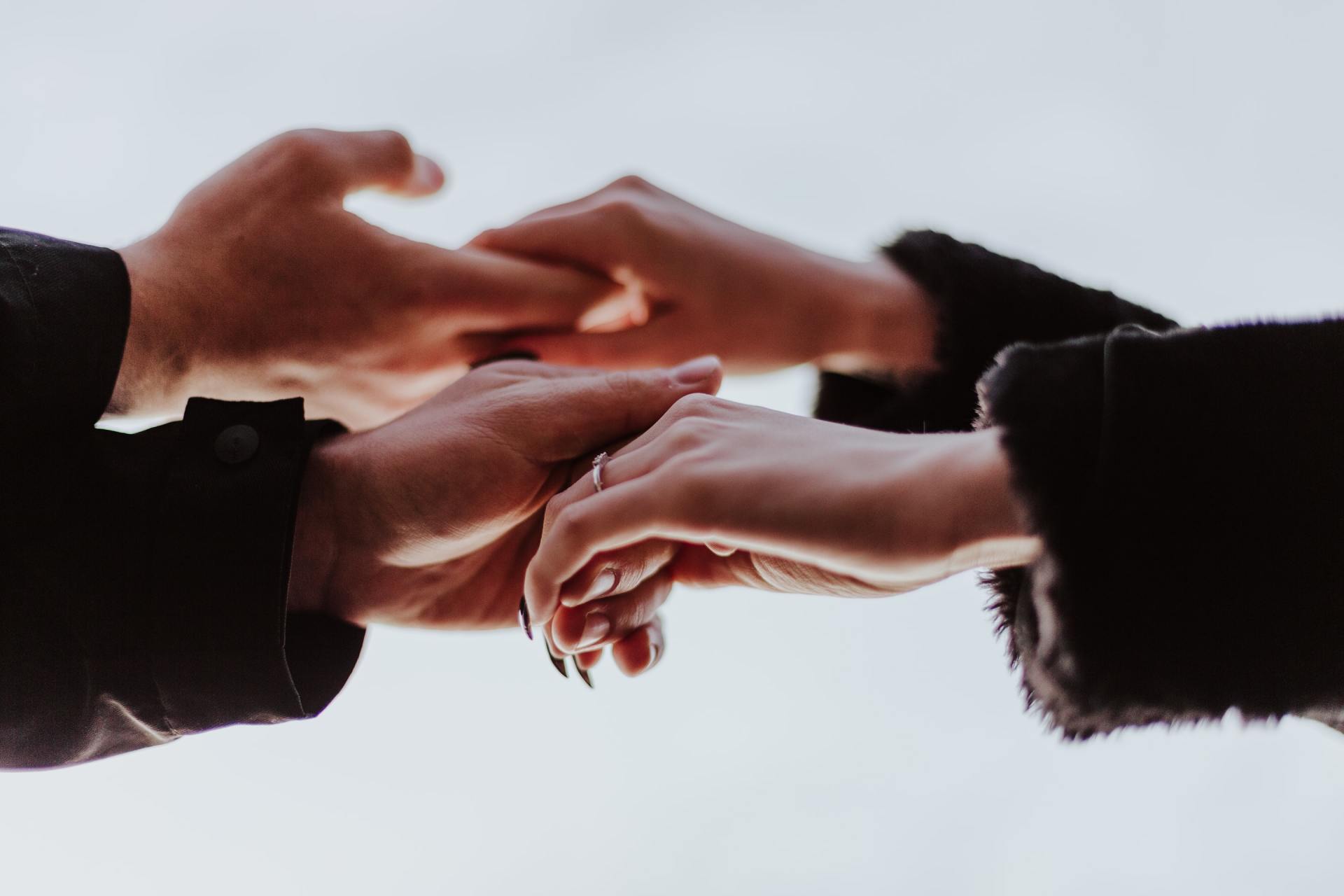 A man and a woman are holding hands and the woman is wearing a wedding ring.