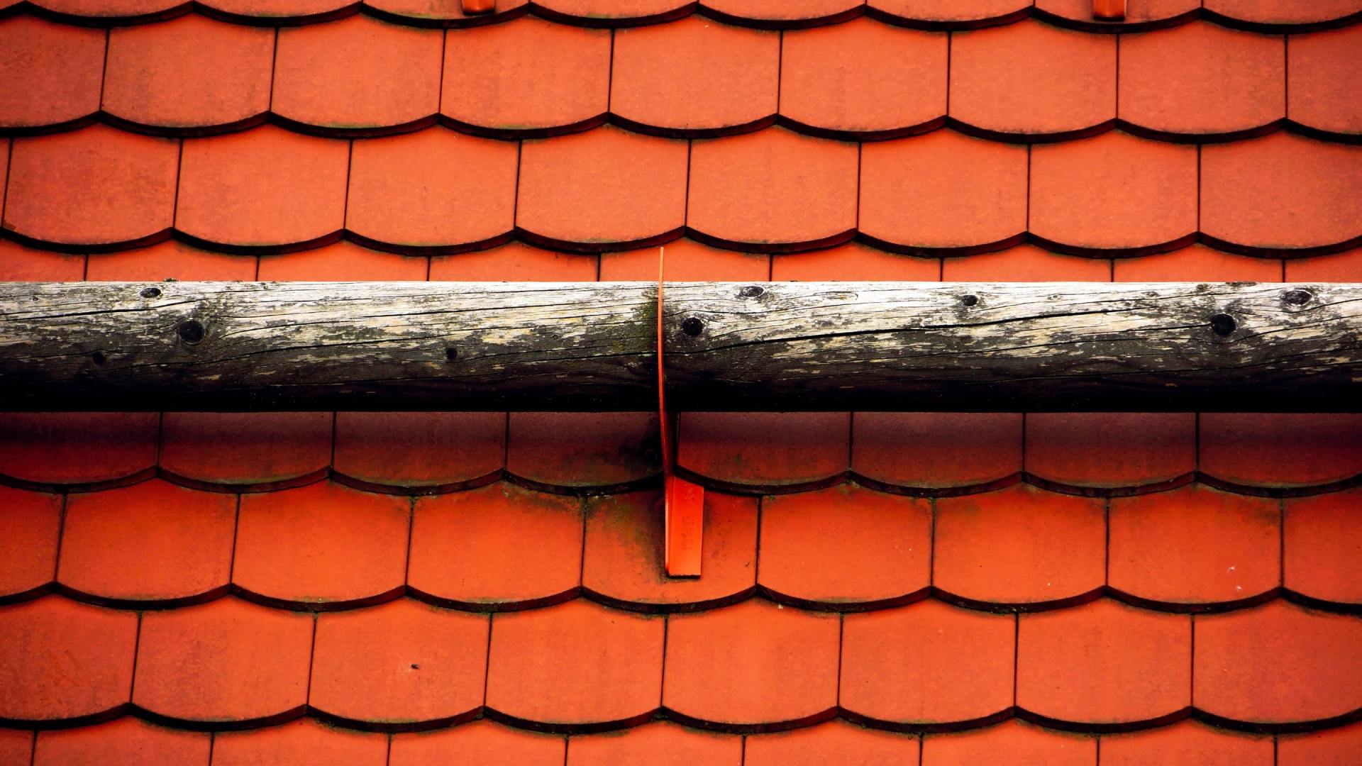 a close up of a roof with red tiles and a wooden gutter .