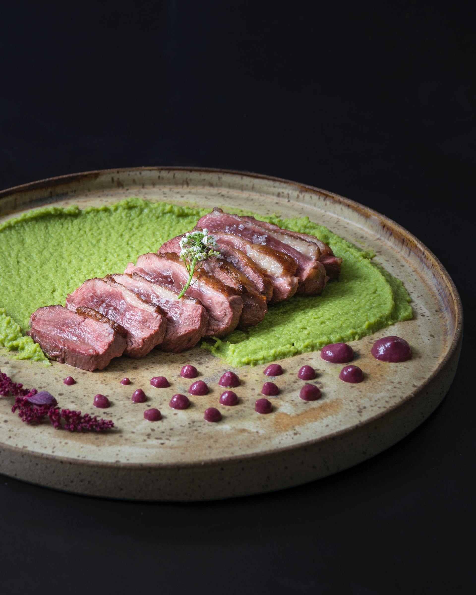 A plate of food with meat and green mashed potatoes on a table.