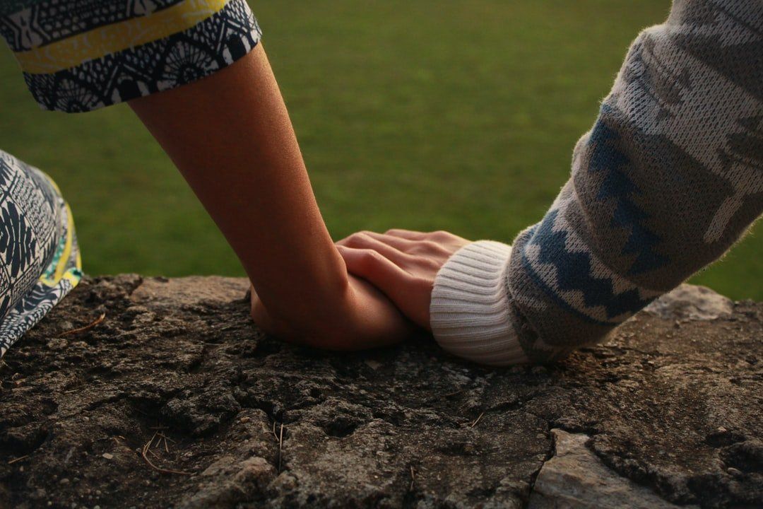 Close up of a woman's hand on a large rock with a man's hand gently on top of her hand.