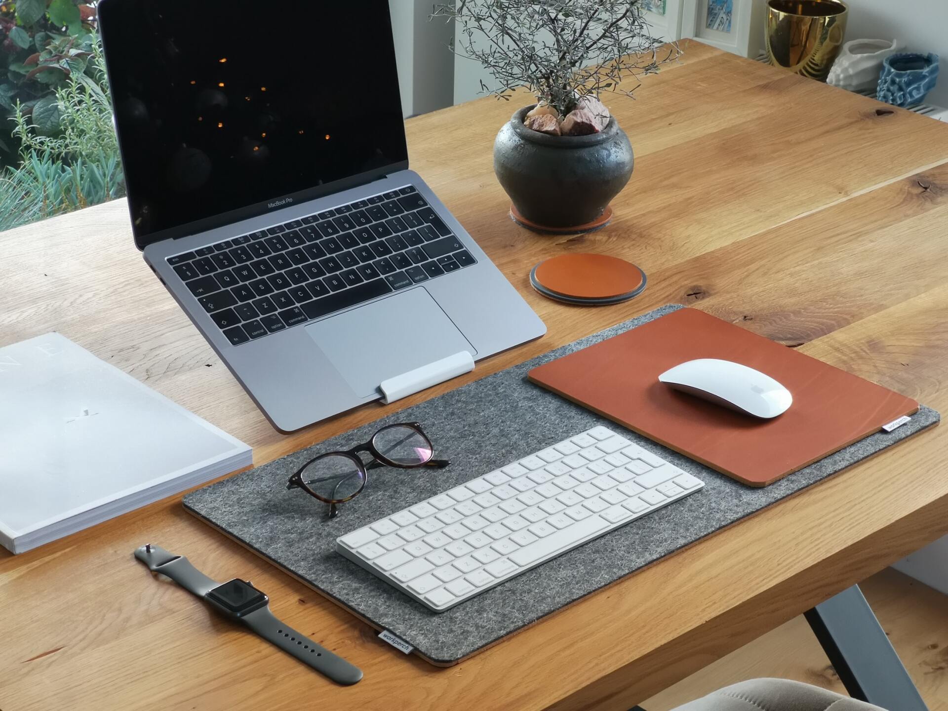 een houten bureau met daarop een laptop, toetsenbord, muis en horloge