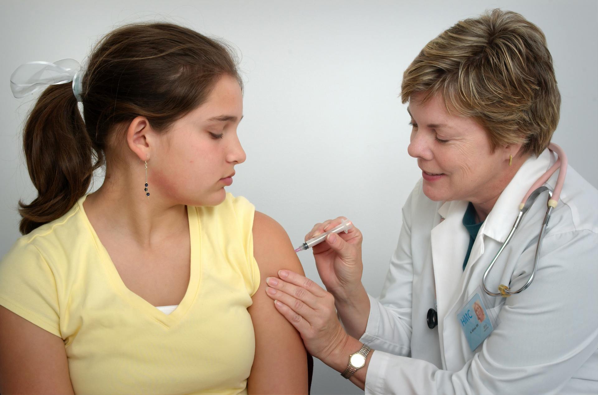 middle aged doctor administering a shot to a young girl in her left arm
