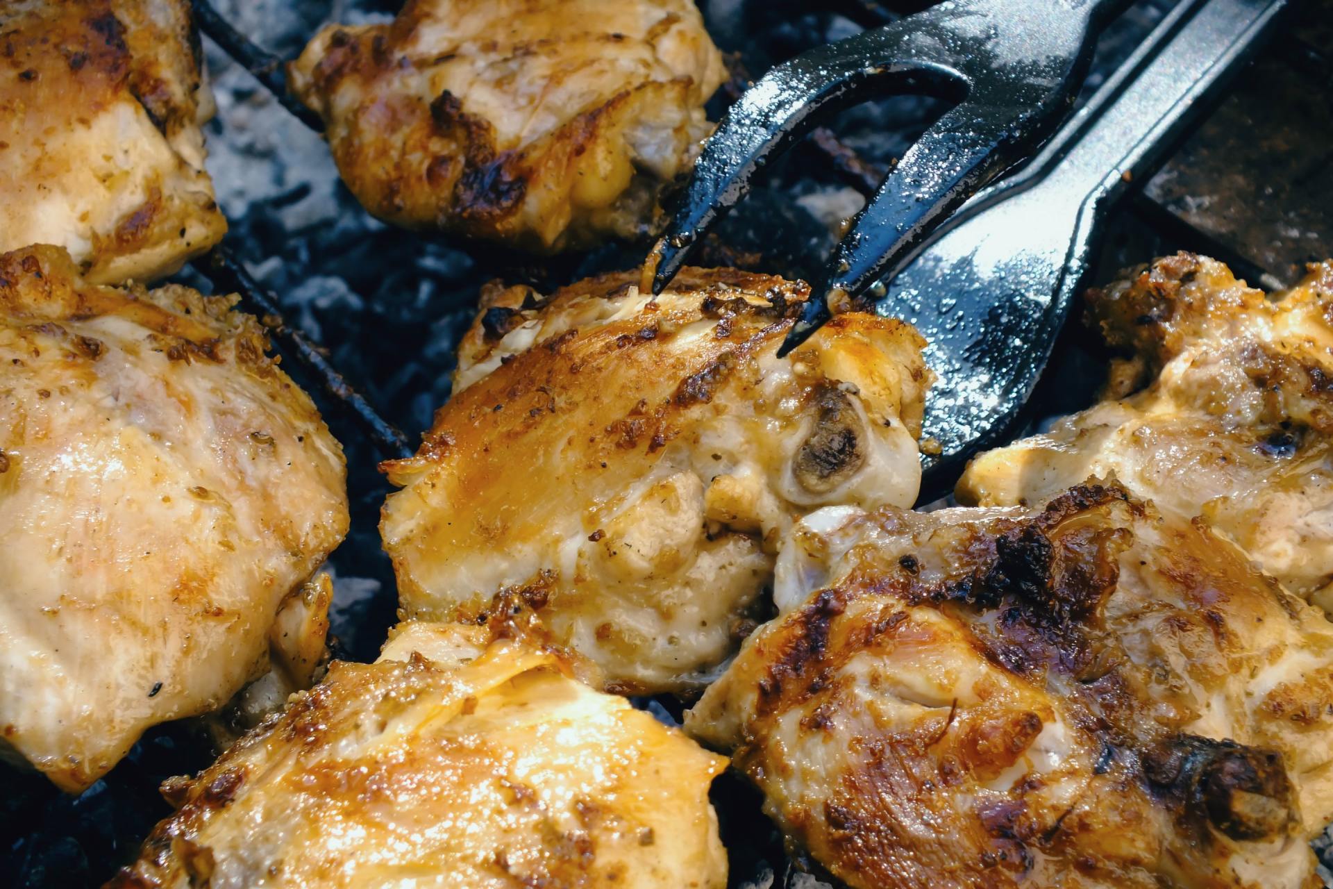 Chicken thighs are being cooked on a grill with a spatula.
