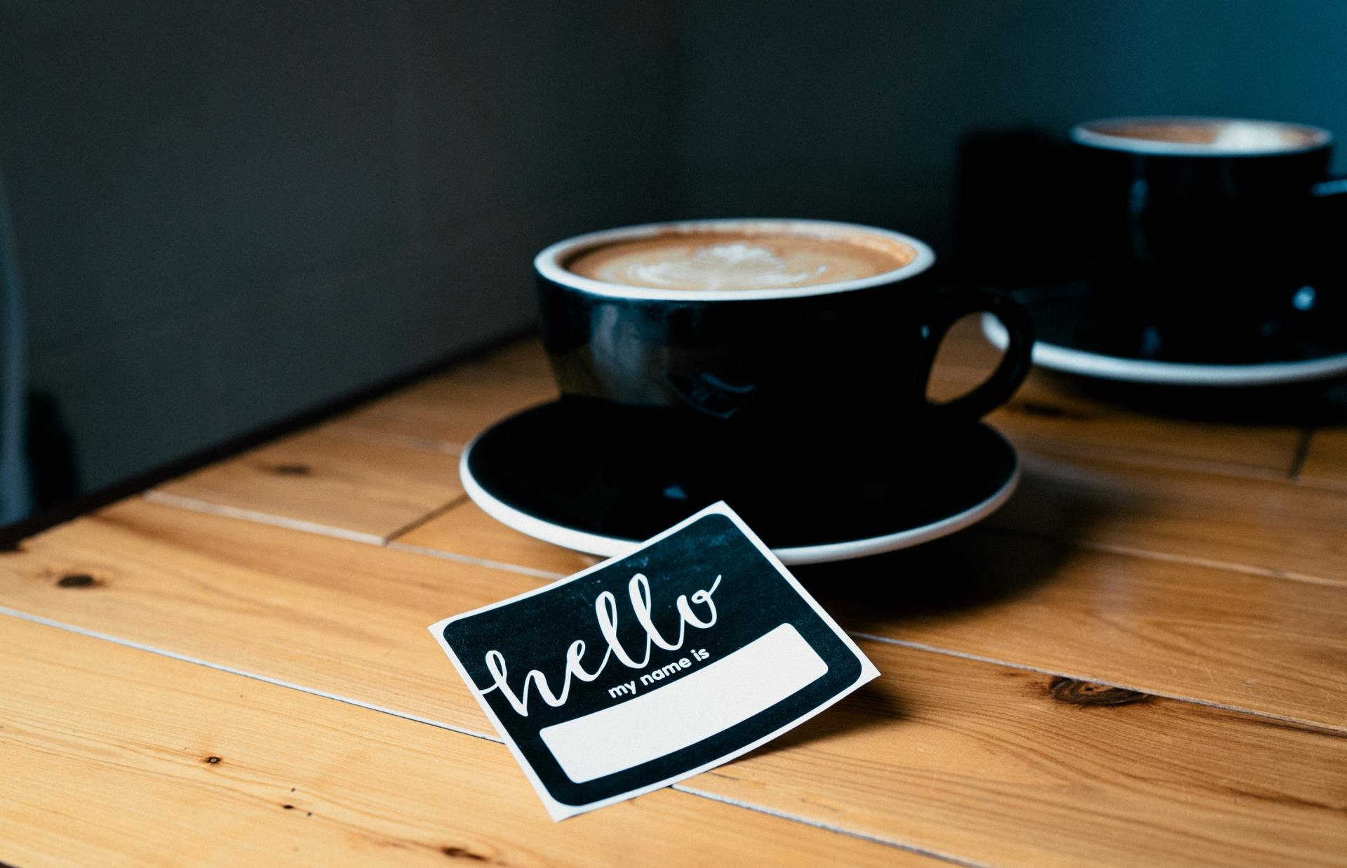 A cup of coffee and a name tag on a wooden table.