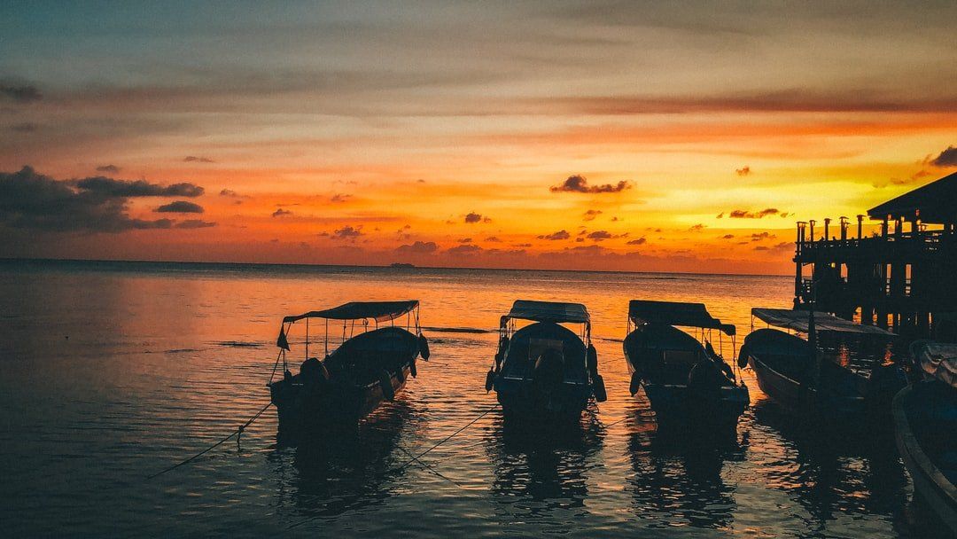 Boats silhouetted on water against an orange sunset. A pier is visible on the right.