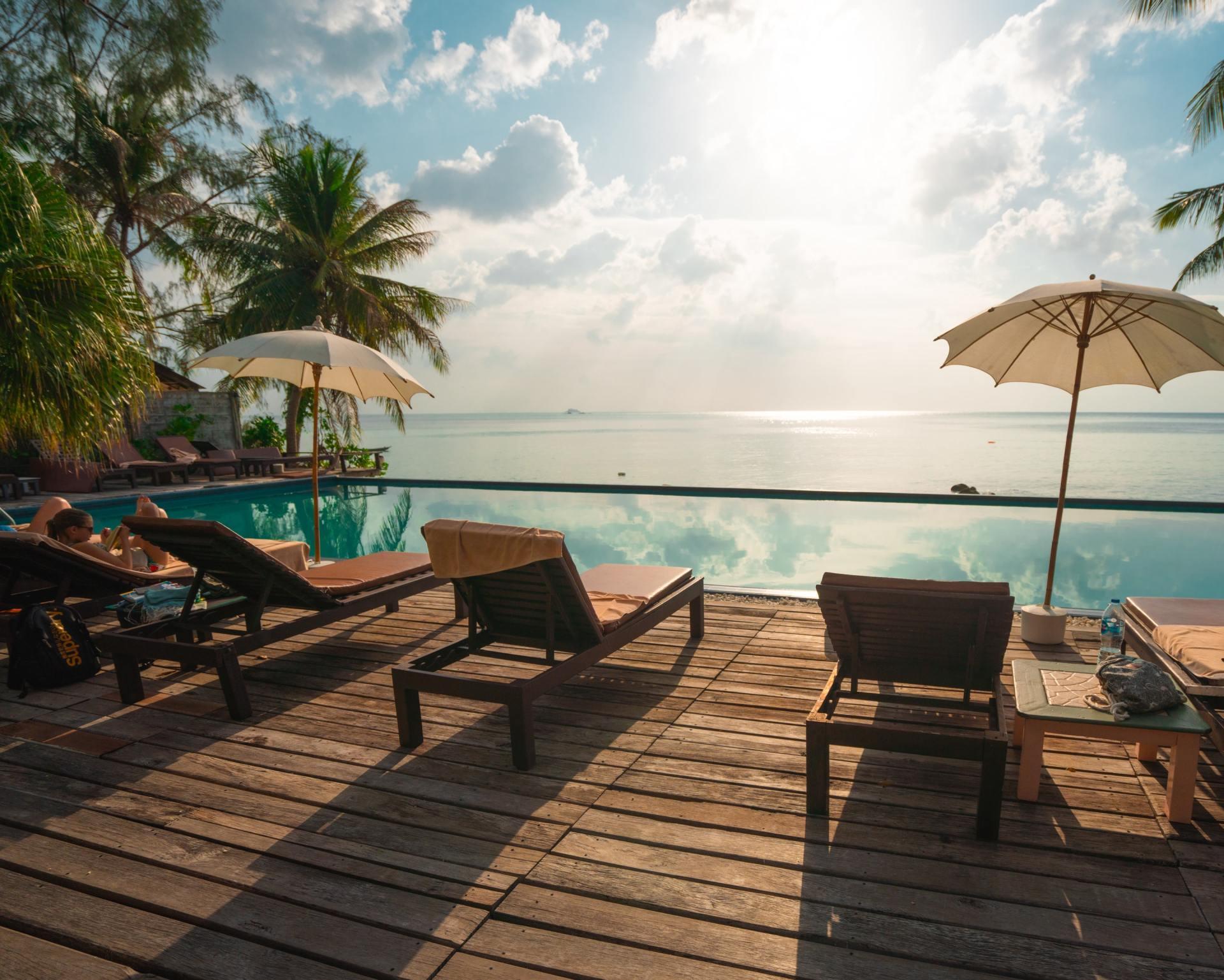 A wooden deck with chairs and umbrellas next to a swimming pool overlooking the ocean.