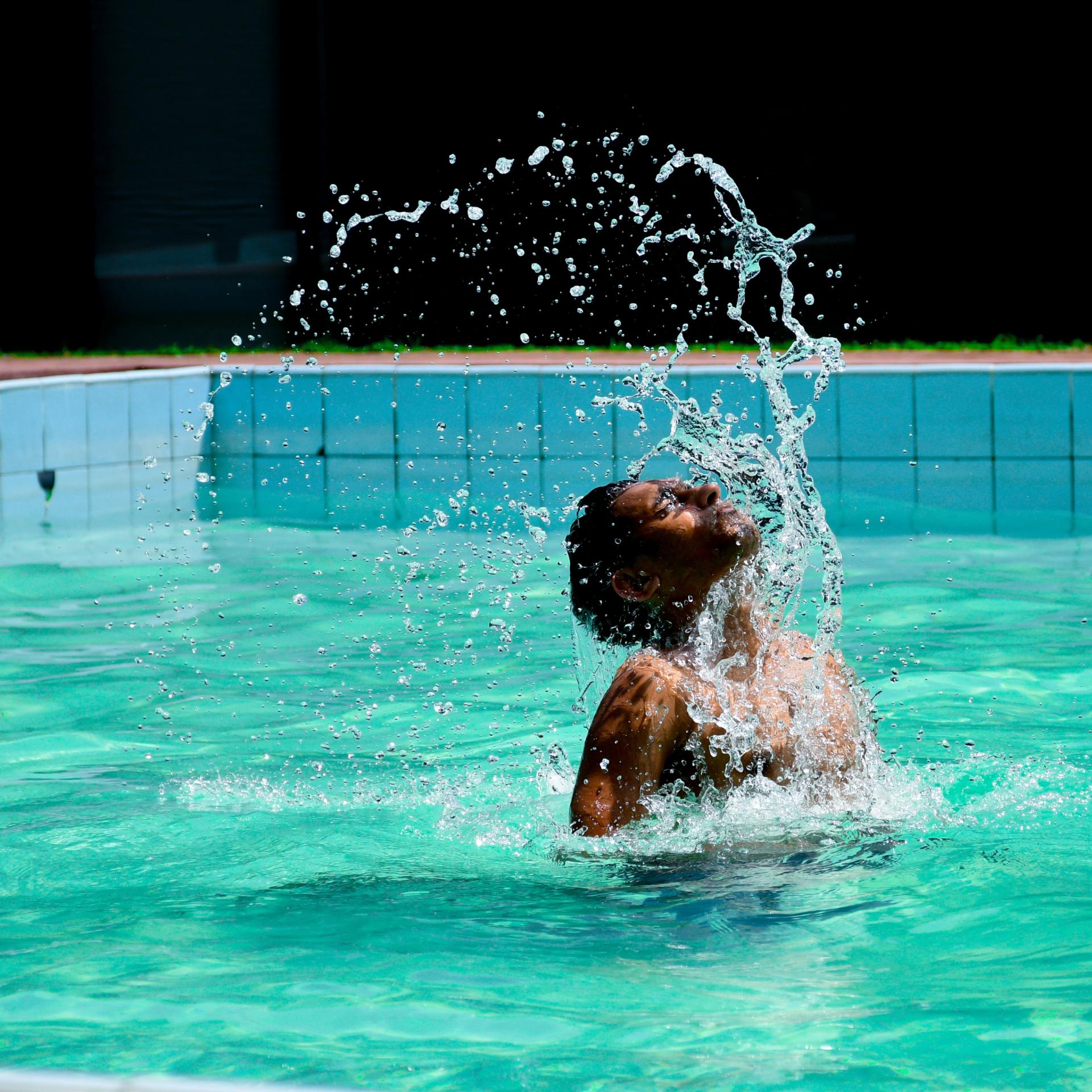 Man havin fun splashing water into the air as he swims in clear blue water surrounded by a blue tiled pool.