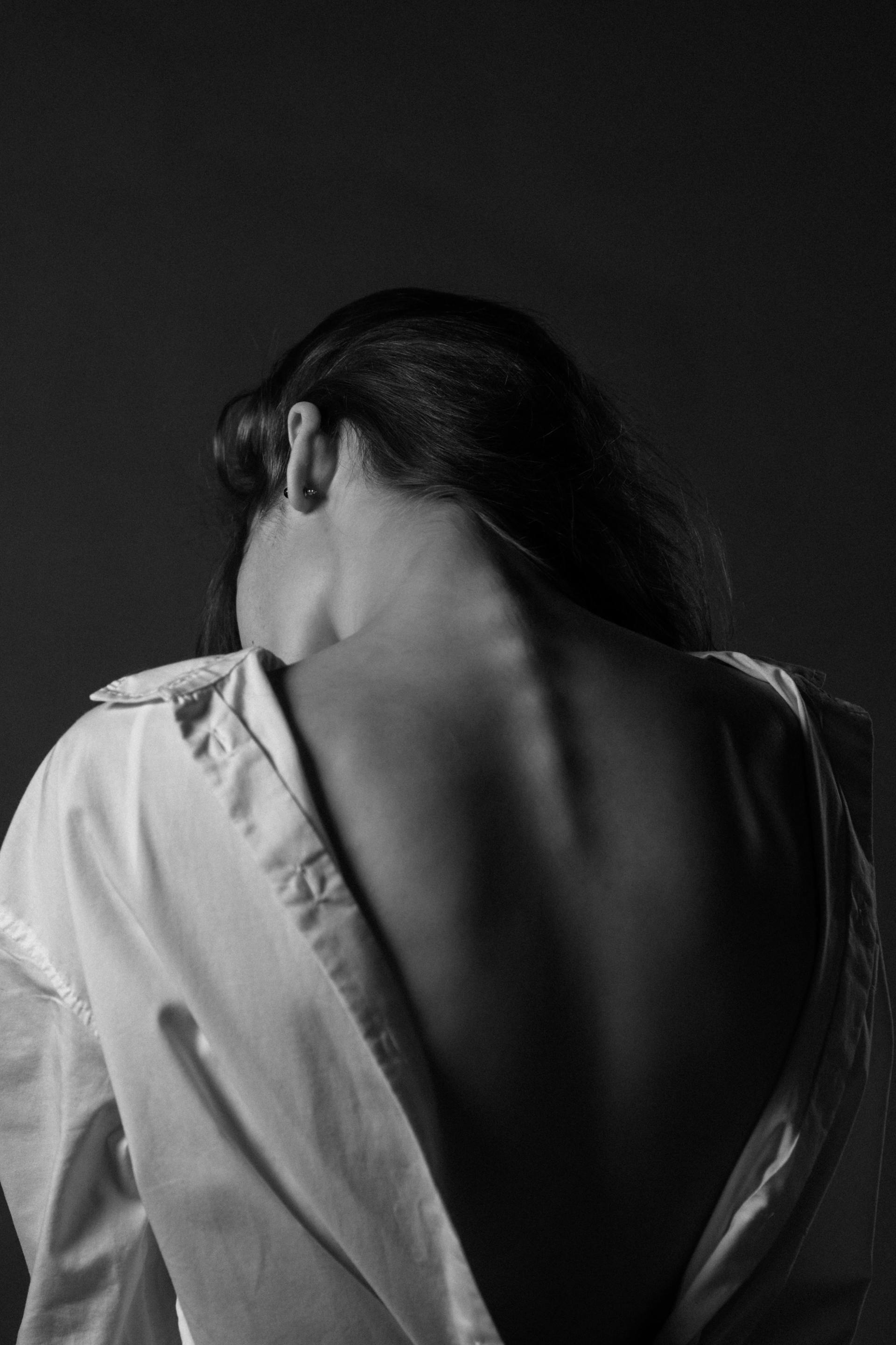 Woman's back in a partially unbuttoned white shirt, back towards the viewer, black and white photo.