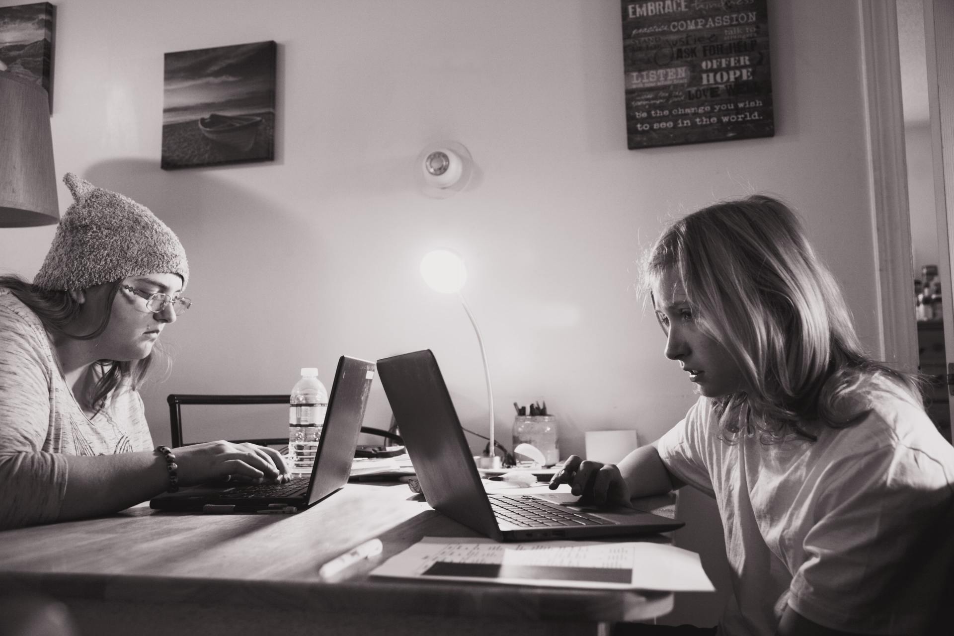 Two women are sitting at a table using laptops.