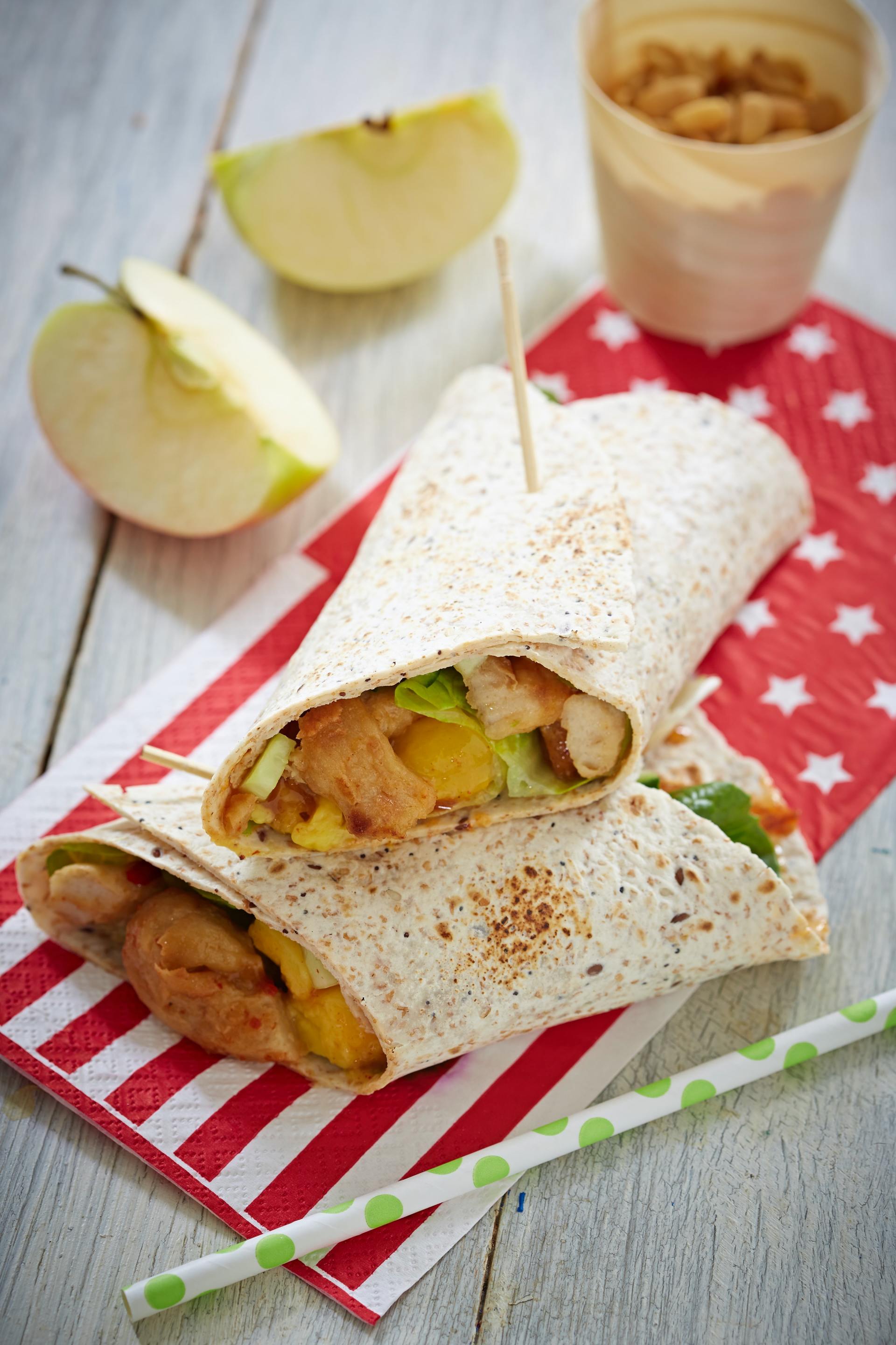 A tortilla wrap with chicken and apples on a napkin on a table.