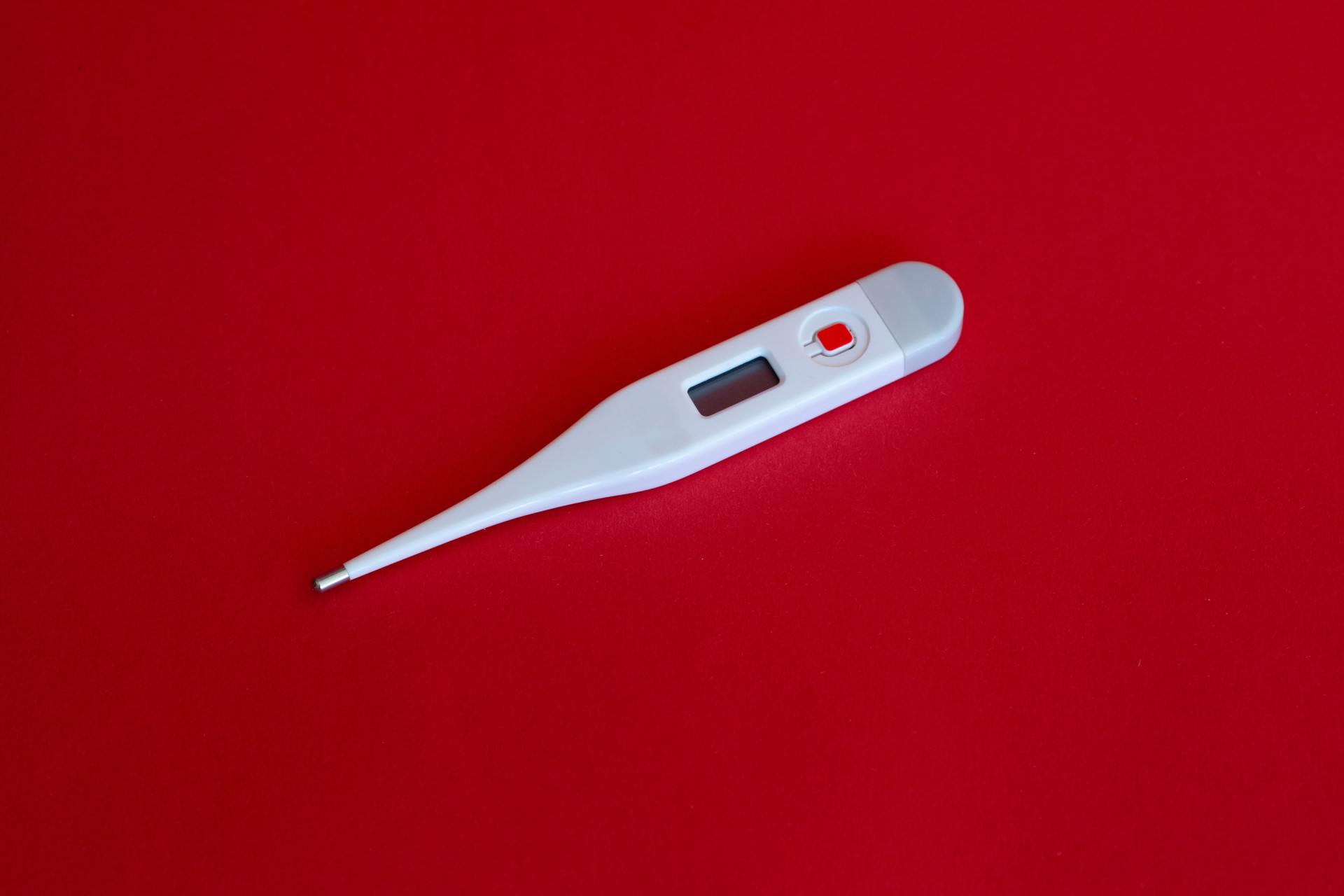 Digital thermometer on red background representing fever symptoms common in Adult-Onset Still's Disease