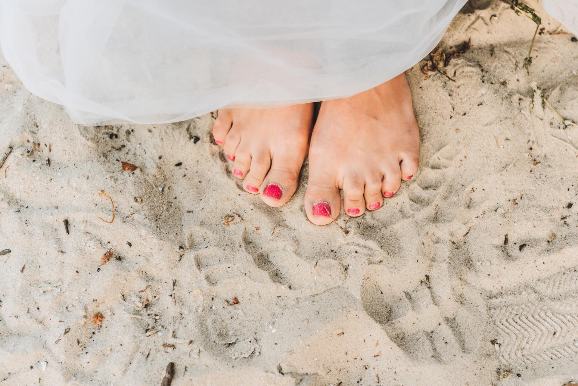 A woman 's feet with pink nail polish are standing in the sand.