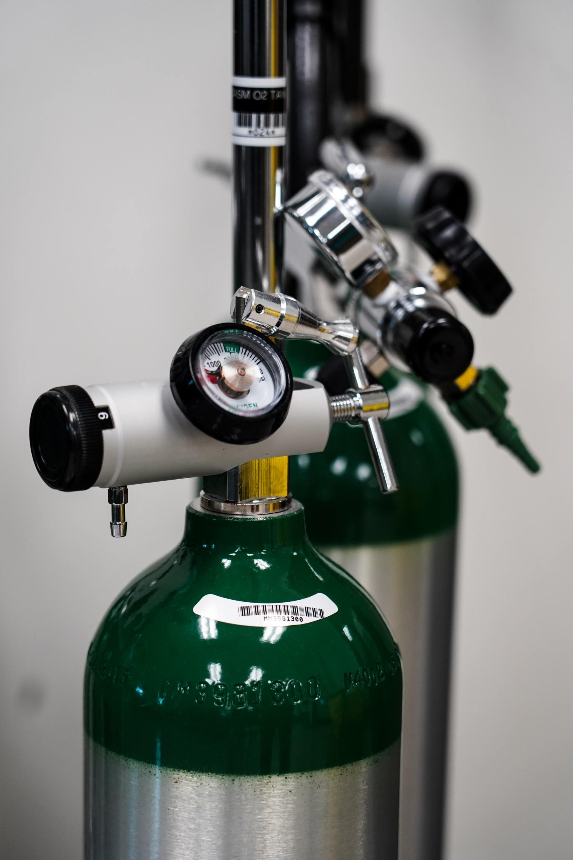 Green and silver oxygen tanks with gauges and regulators, lined up against a white wall.