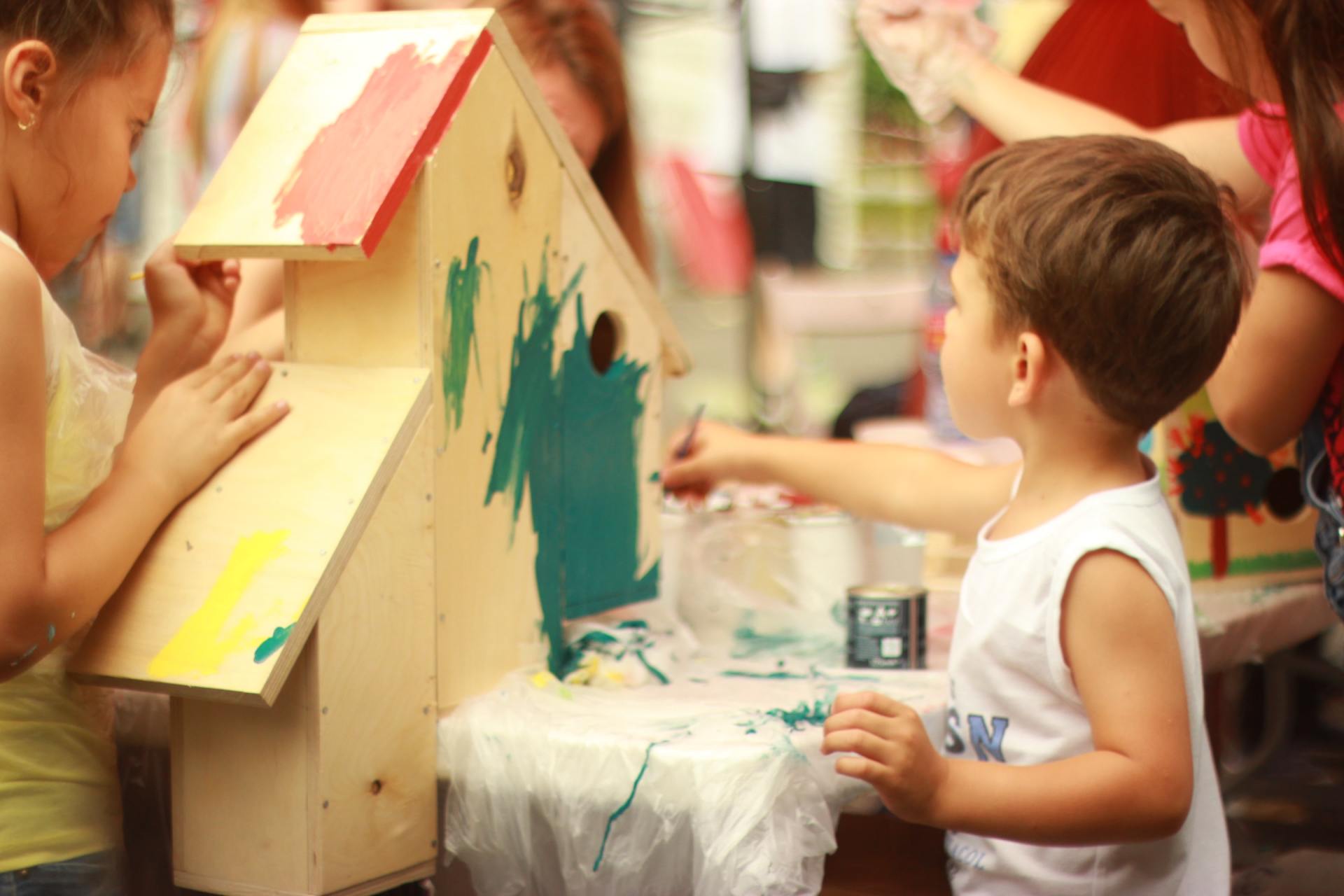 Young boy painting a small wooden bird box with paint