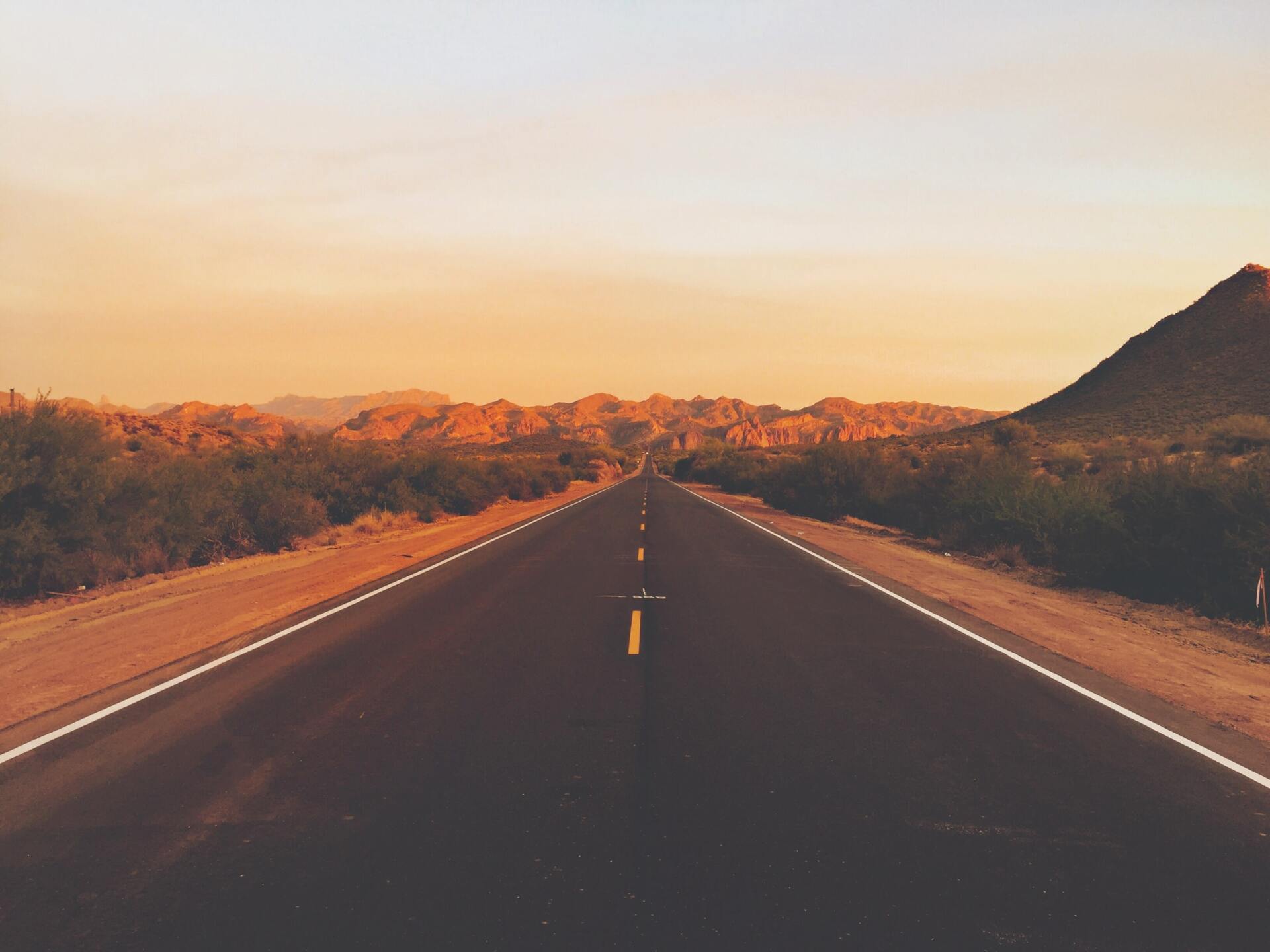 Road stretching toward a mountain range at sunset.