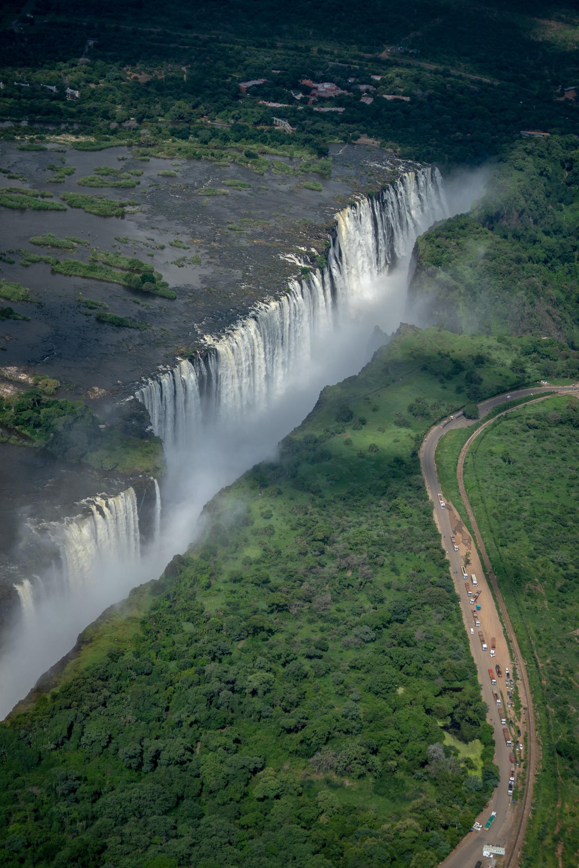 An aerial view of a waterfall surrounded by trees and a road.