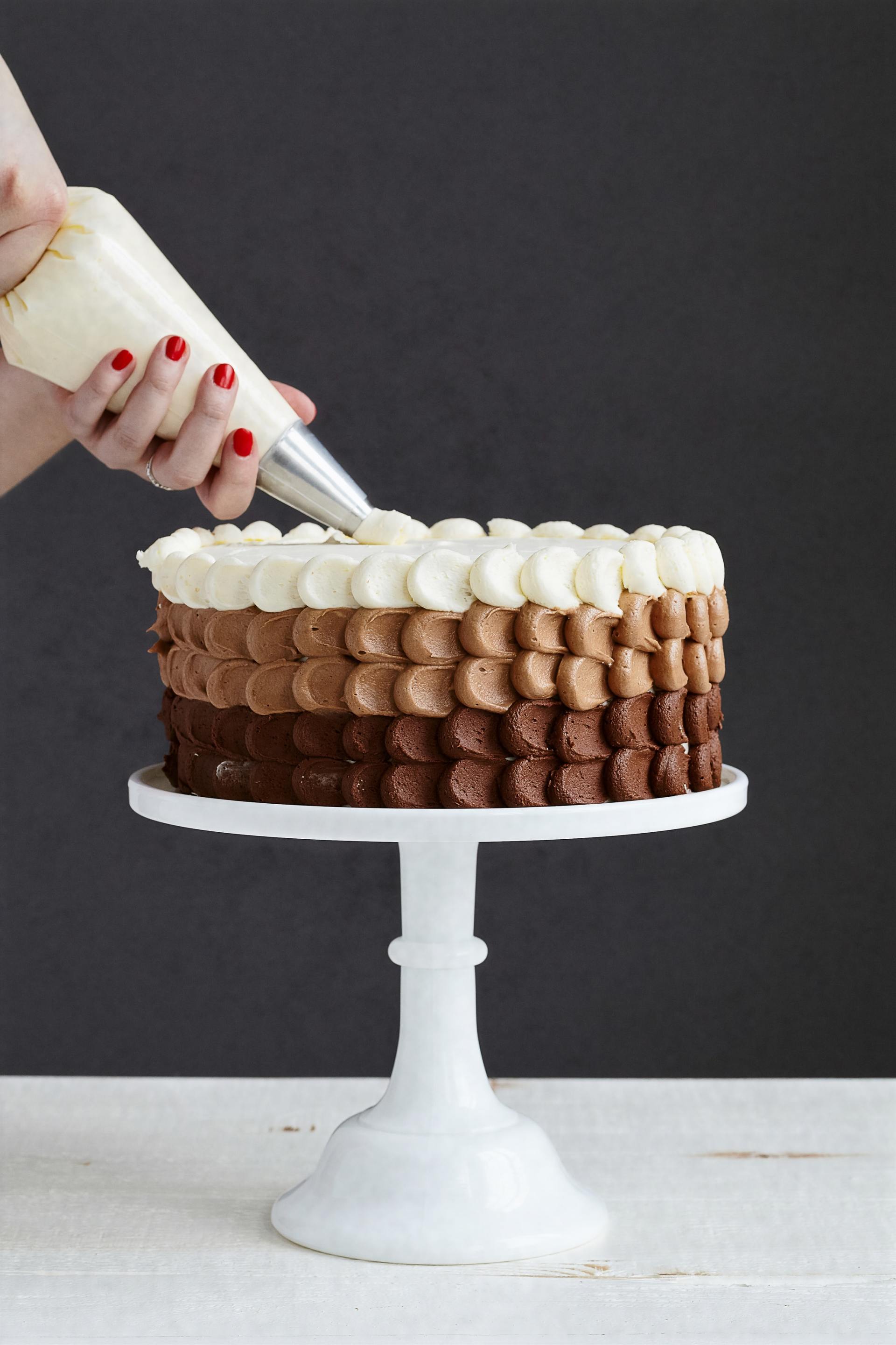 A person is frosting a cake on a white cake stand
