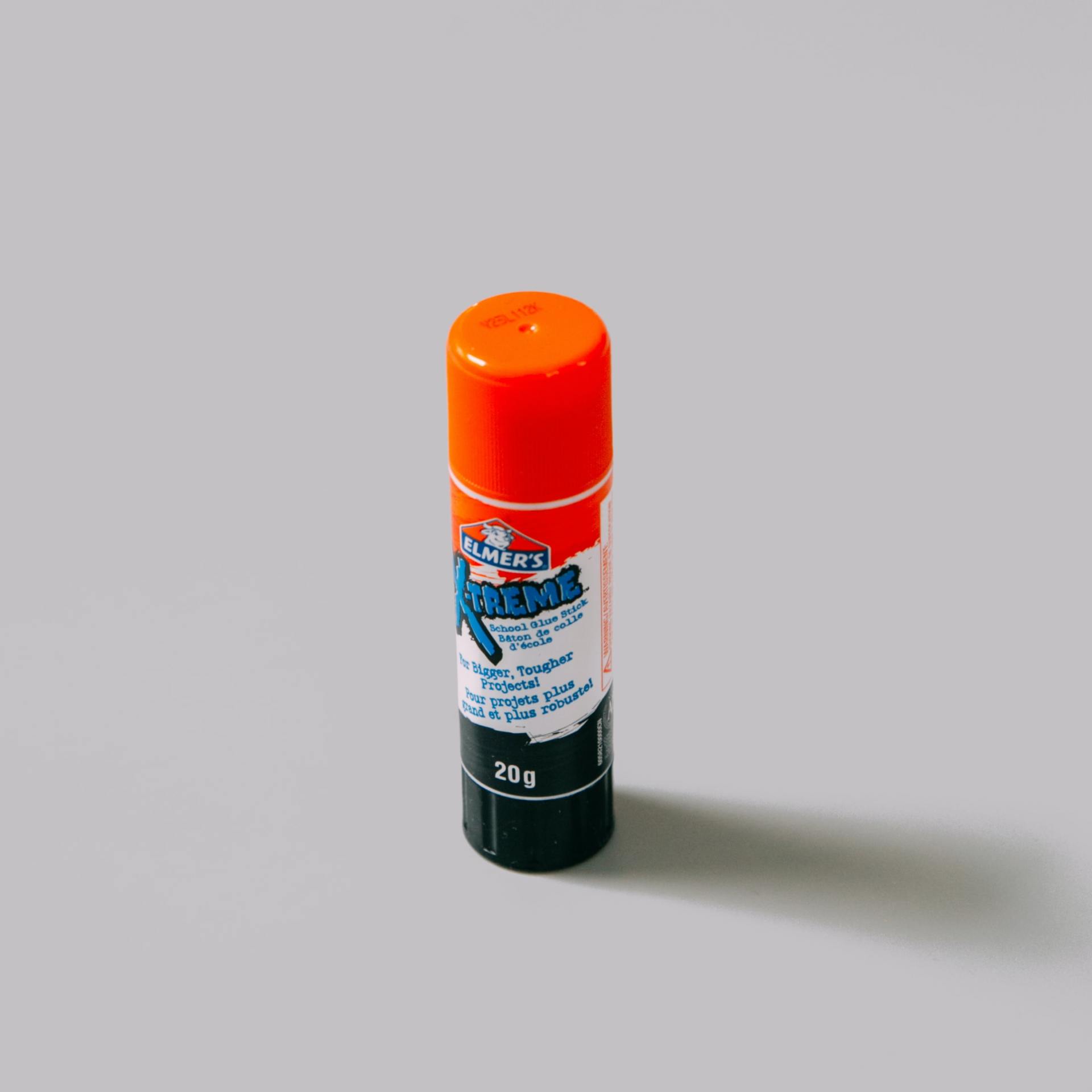 Glue stick with orange cap and black base, standing upright on a grey surface.