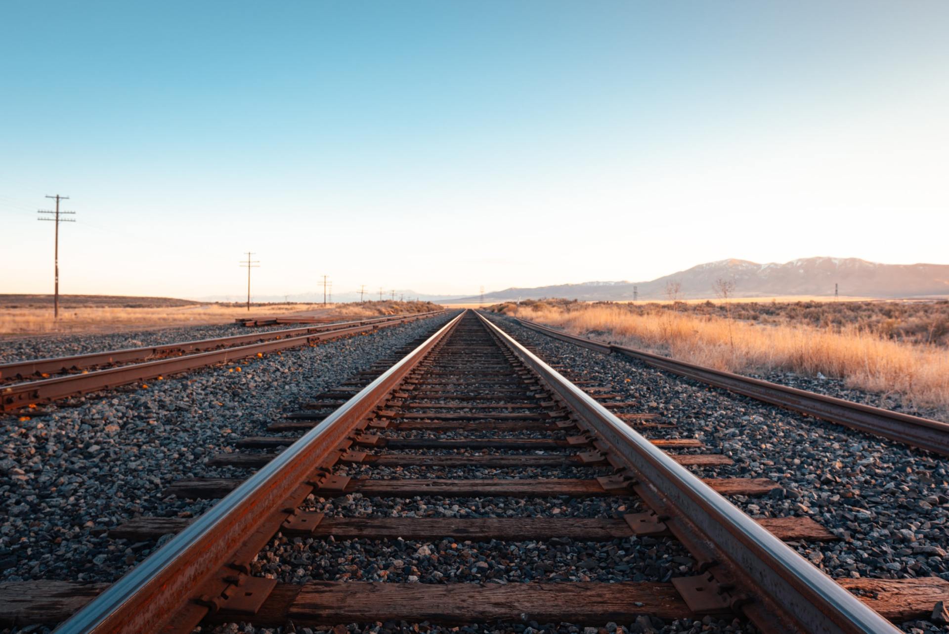 A train track in the middle of a field with mountains in the background.