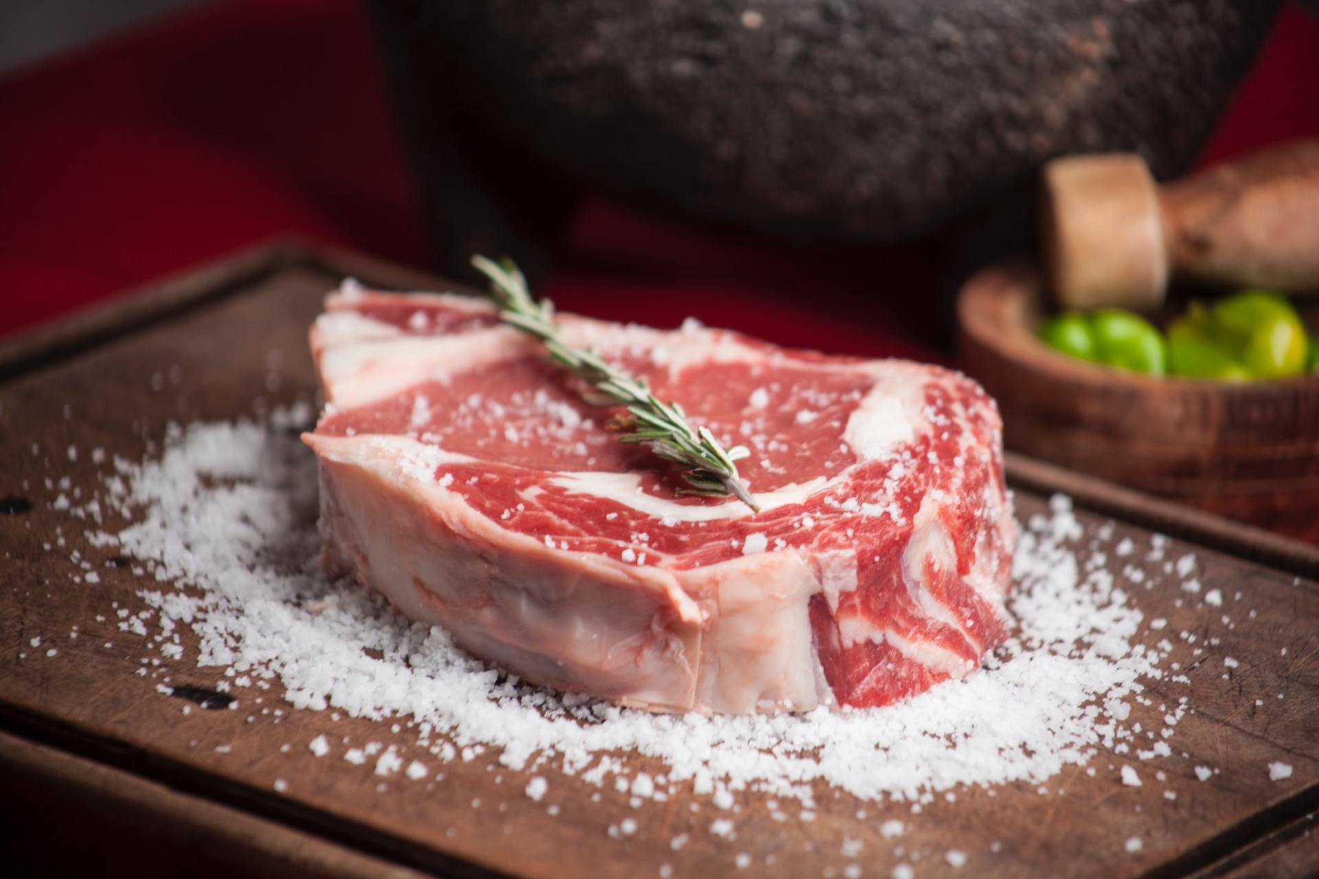 A piece of raw meat is sitting on top of a wooden cutting board covered in salt.