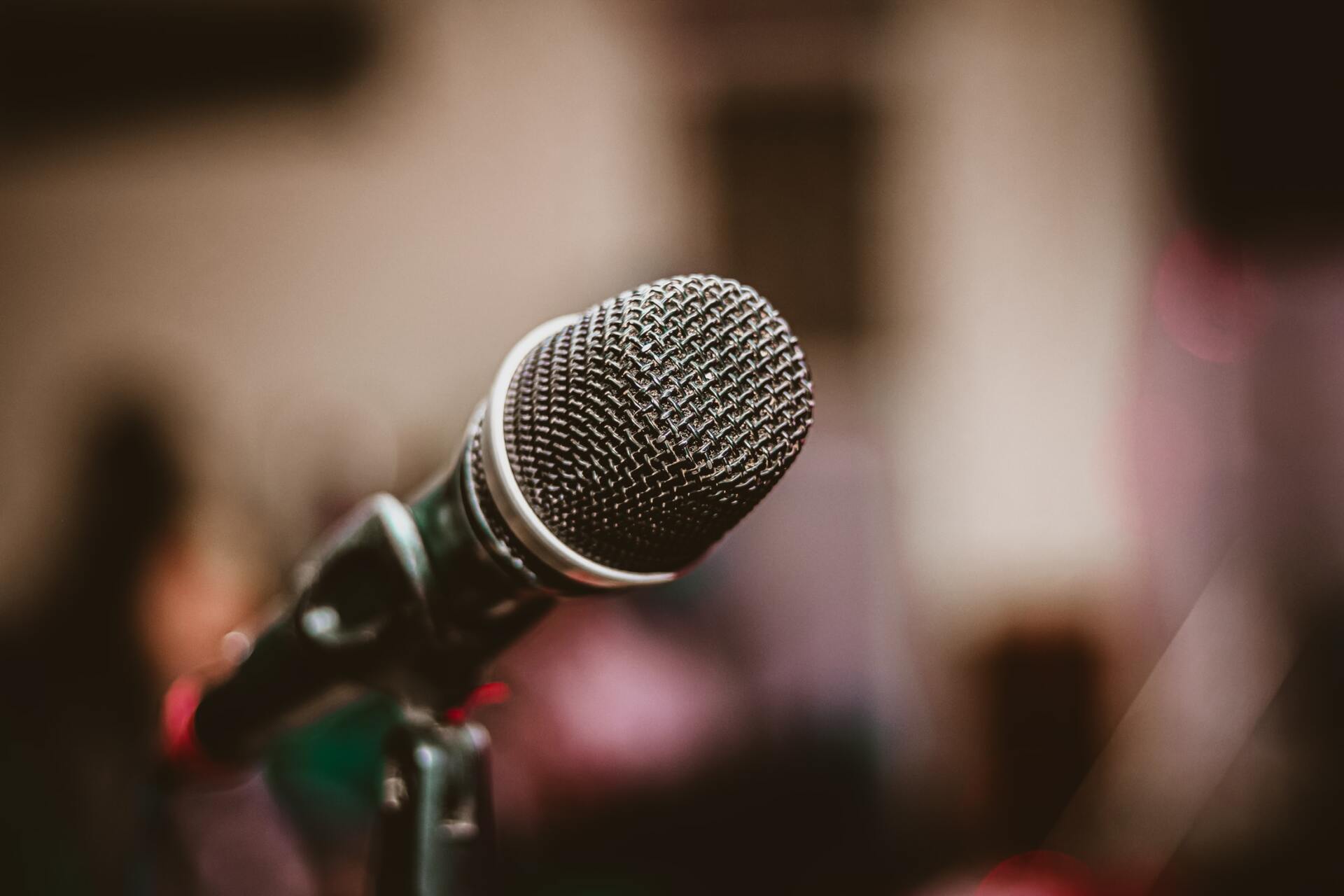 Close-up of a black microphone on a stand with a blurred background, likely a performance venue.